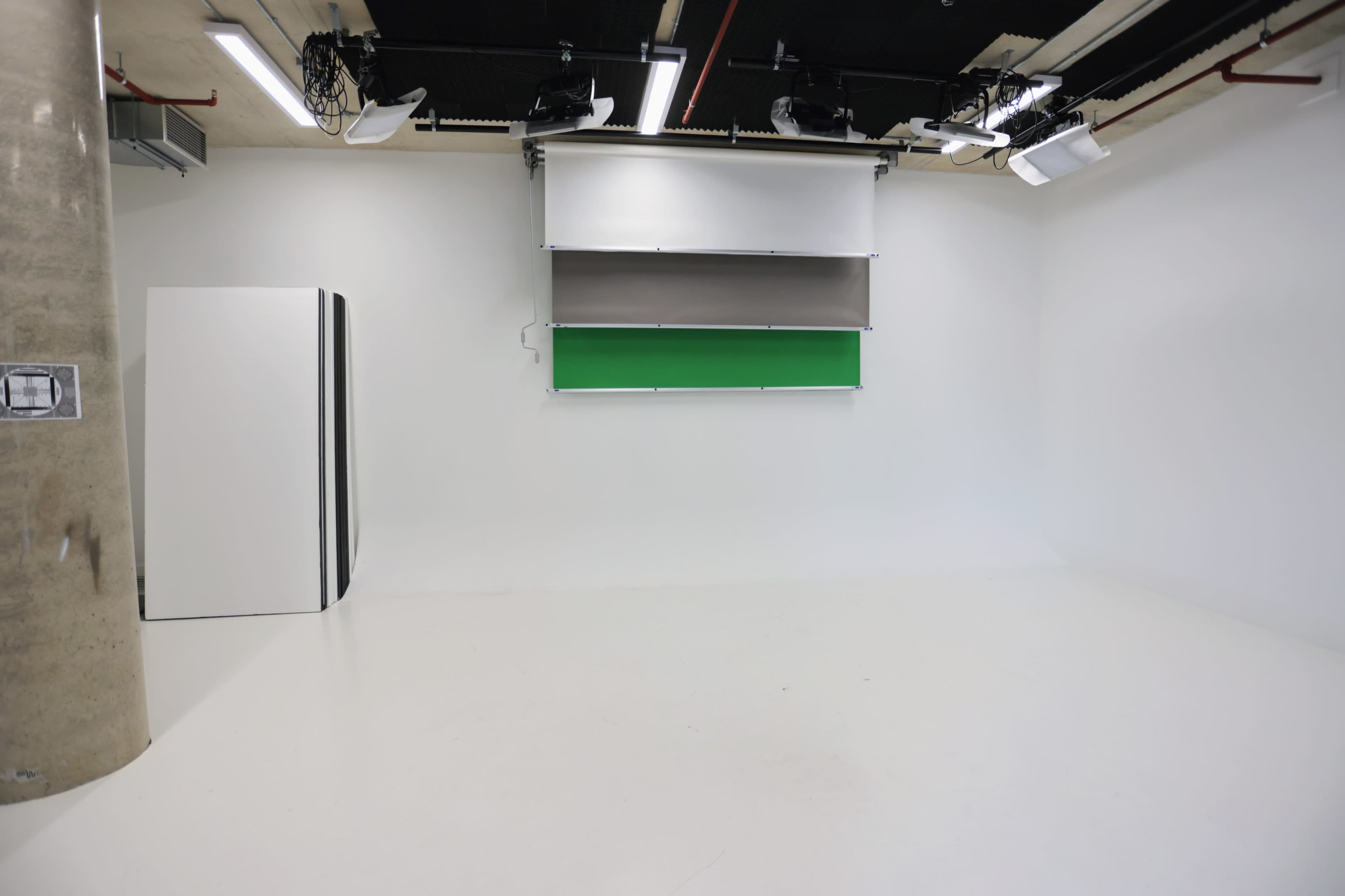 A minimalist studio space with a green screen and a blank white backdrop.