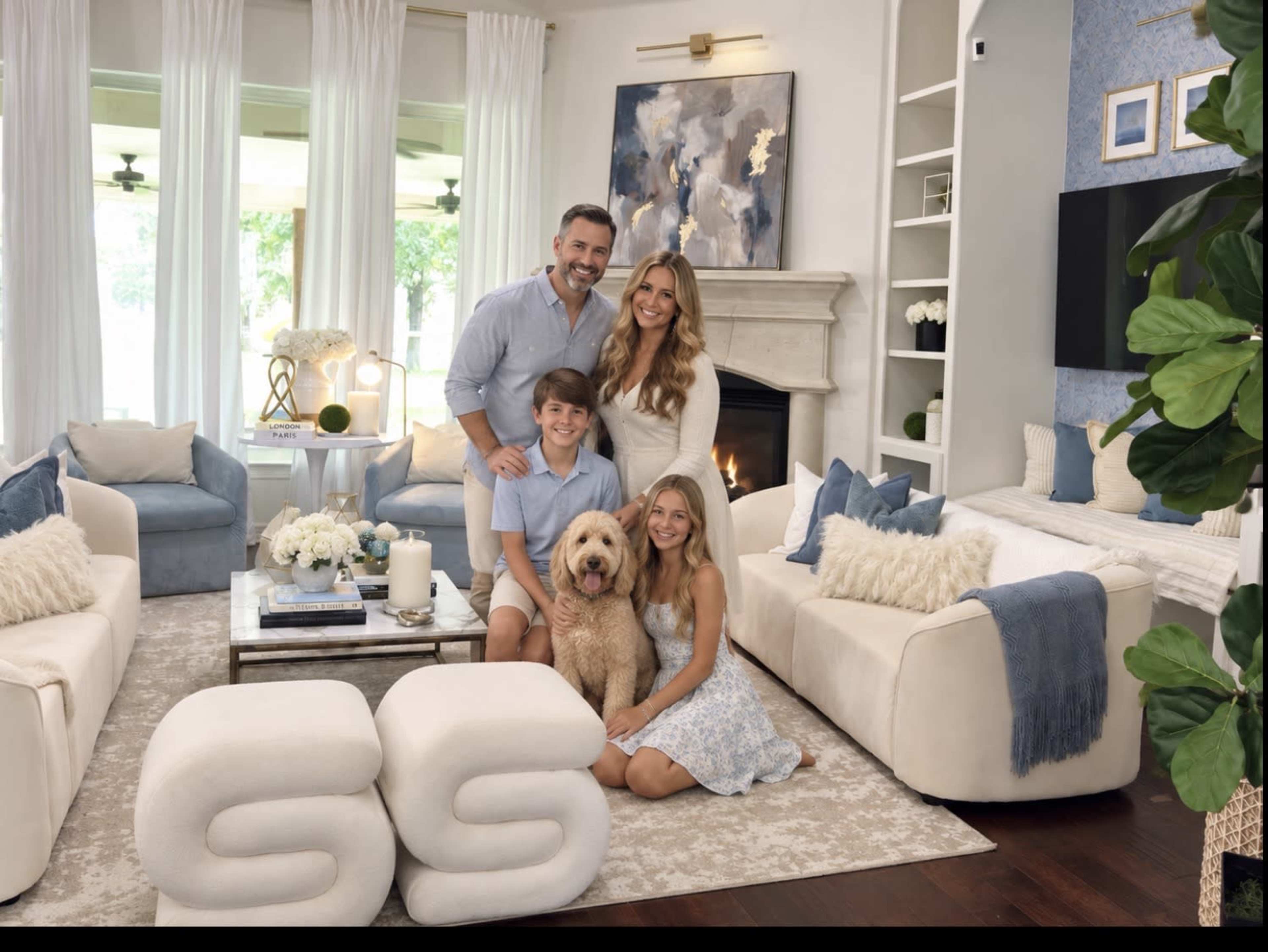 A family of four, along with a dog, poses together in a modern living room featuring white furniture and large windows.