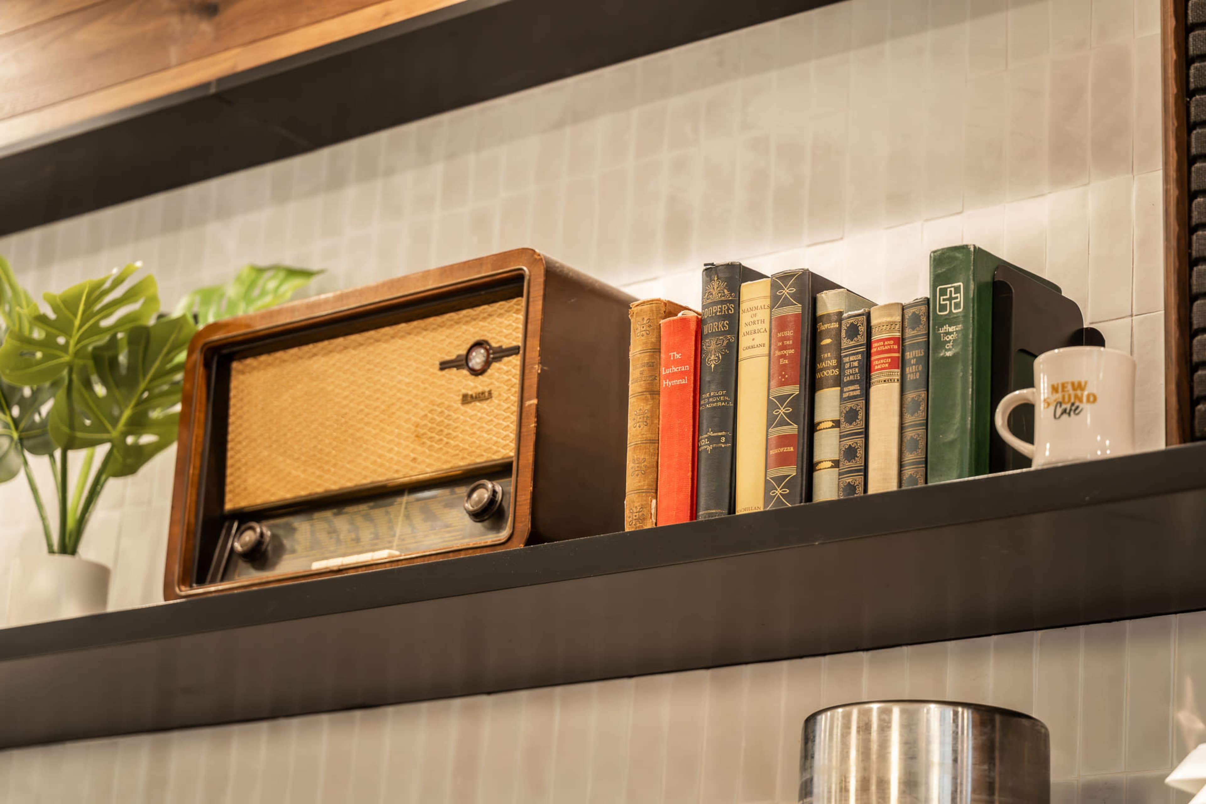 A vintage wooden radio is displayed on a shelf alongside several old books and a small potted plant.