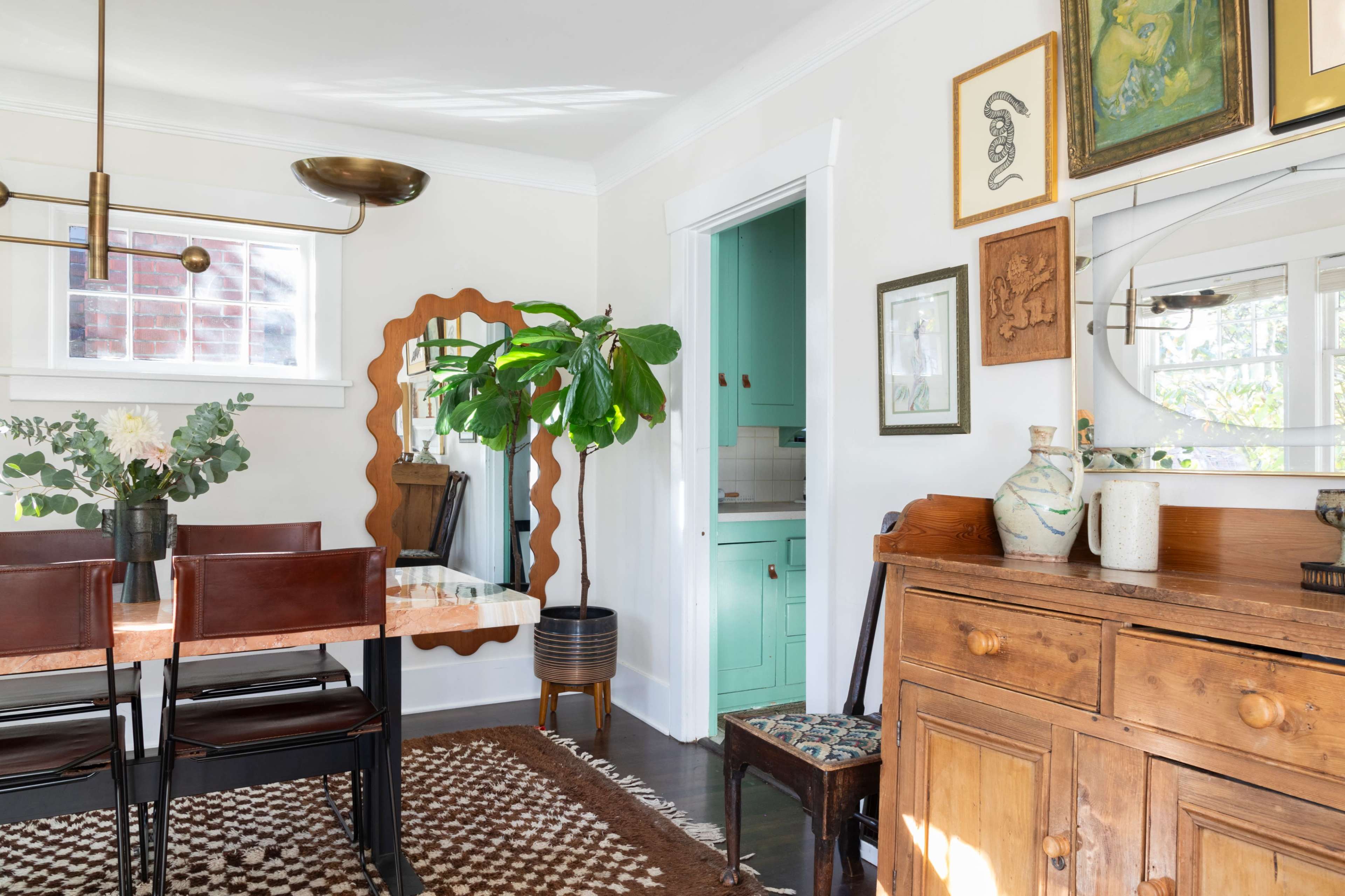 A dining area features a table surrounded by brown leather chairs, a large mirror, a potted plant, and a wooden sideboard with decorative items.