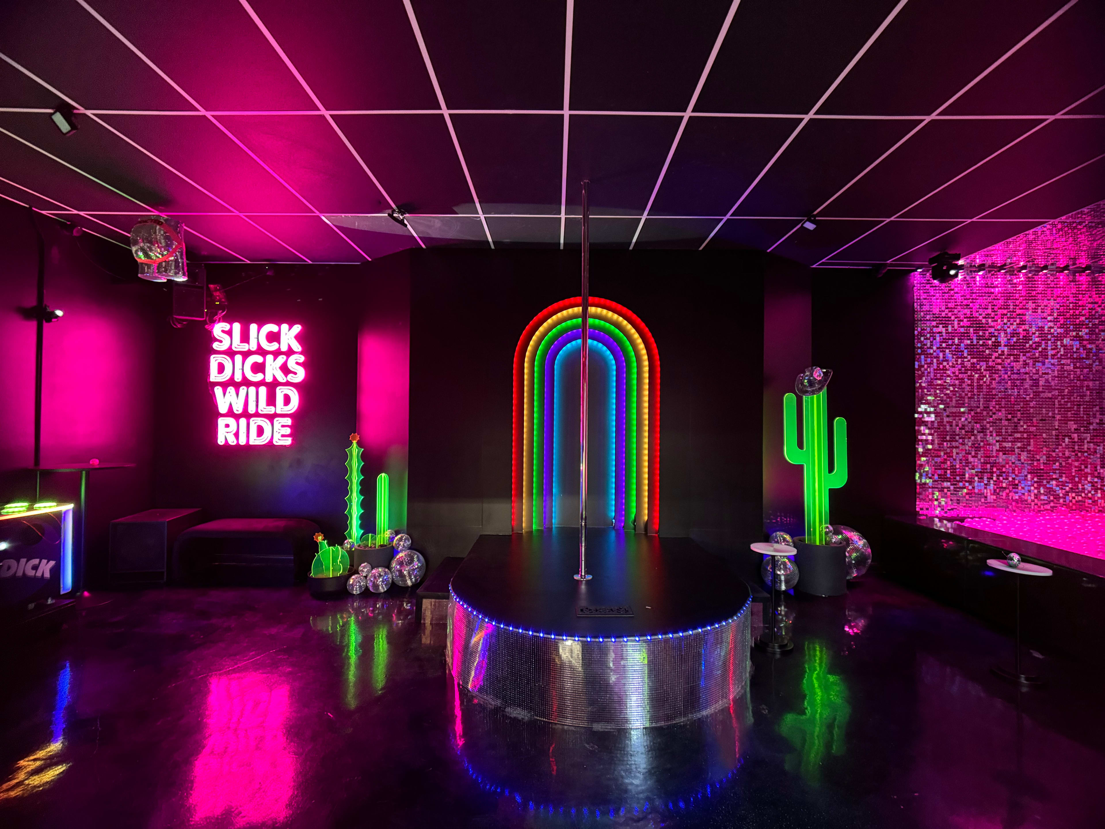 The image shows a vibrant nightclub interior with neon lights, including a rainbow arch, a pole in the center, and decorative elements like cactus figures on the walls.