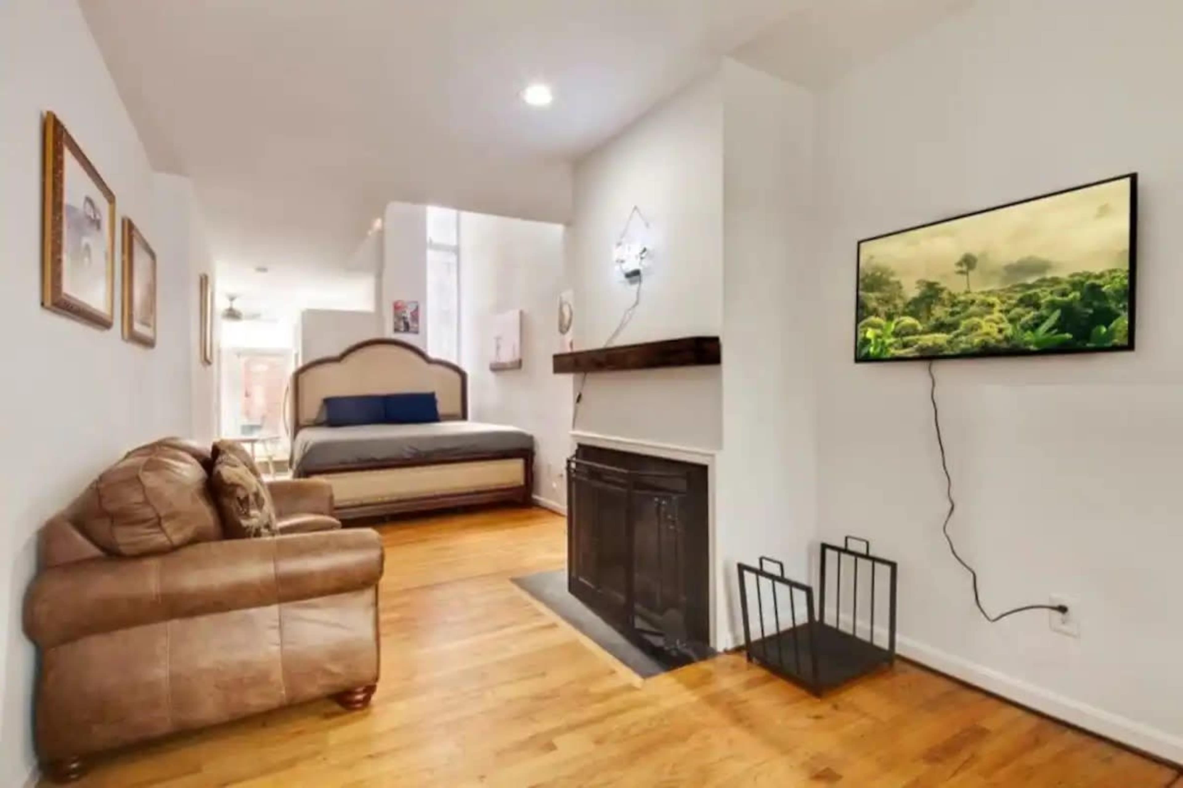 A living space with a sofa, a bed in the background, a wall-mounted television, and a fireplace.