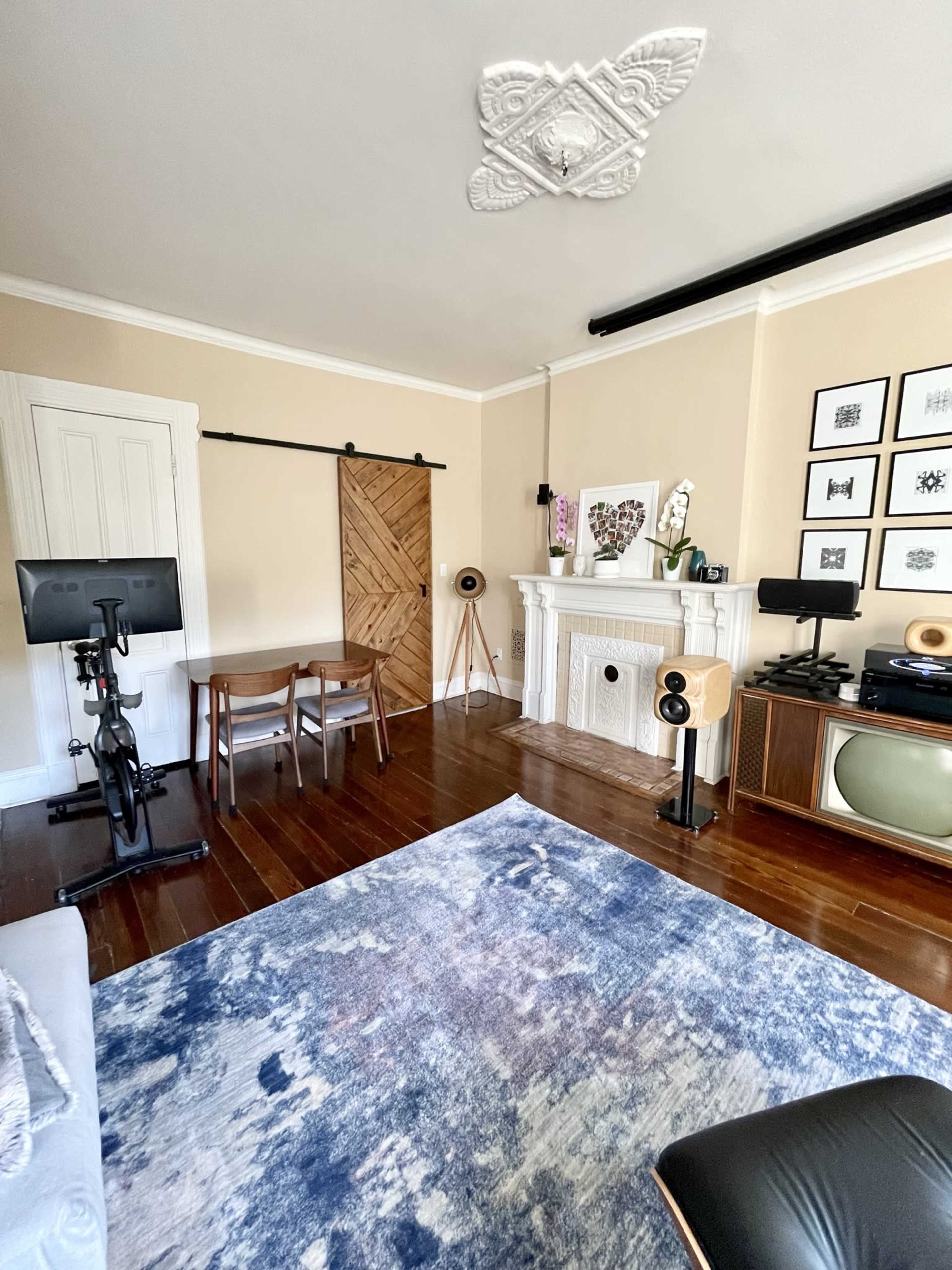 A spacious living room with a wooden floor, featuring a table with chairs, a fireplace, a television, and a wall adorned with framed art.