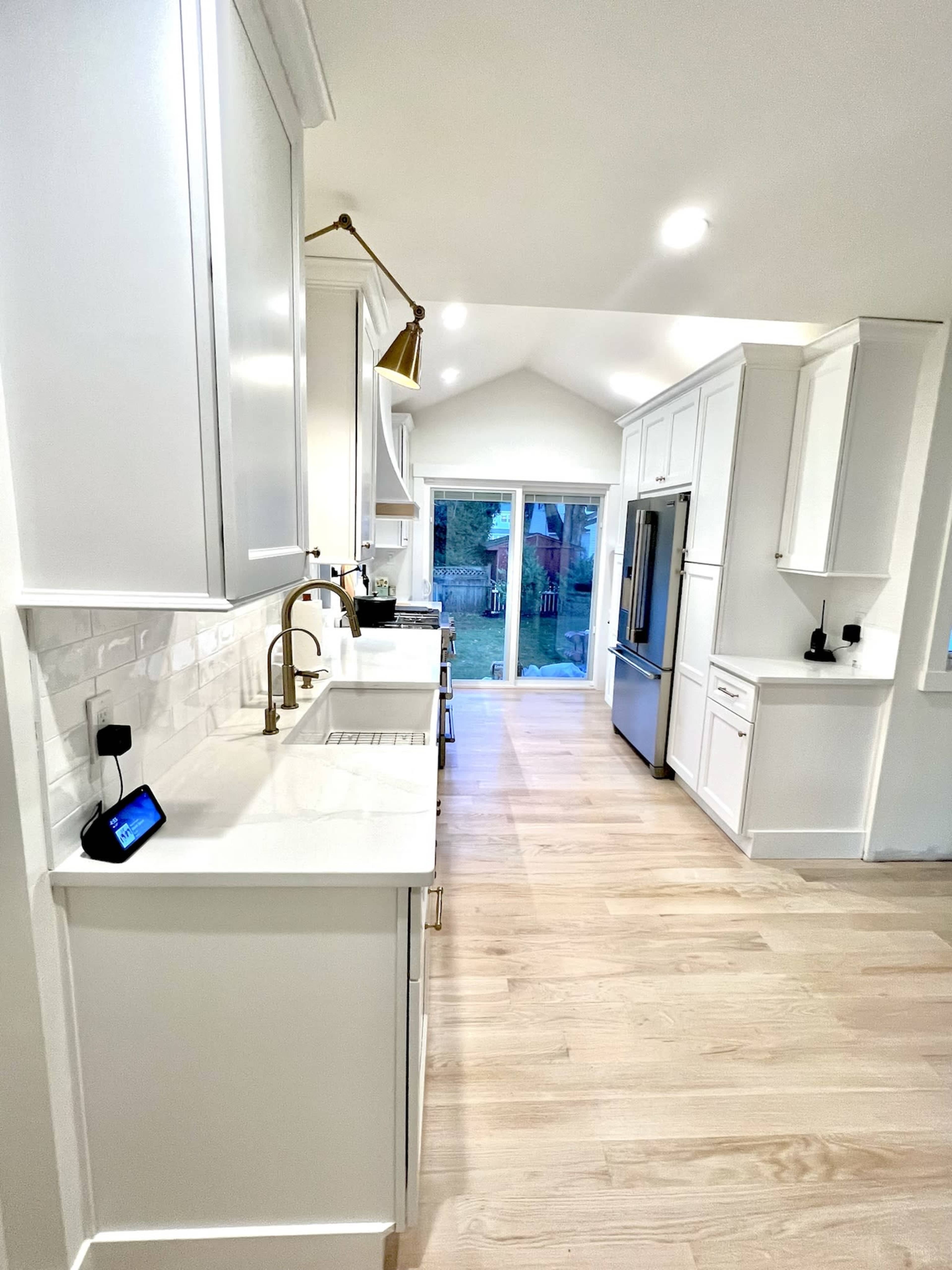 A modern kitchen features white cabinetry, a large sink, and stainless steel appliances, with a view of a patio through a sliding glass door.