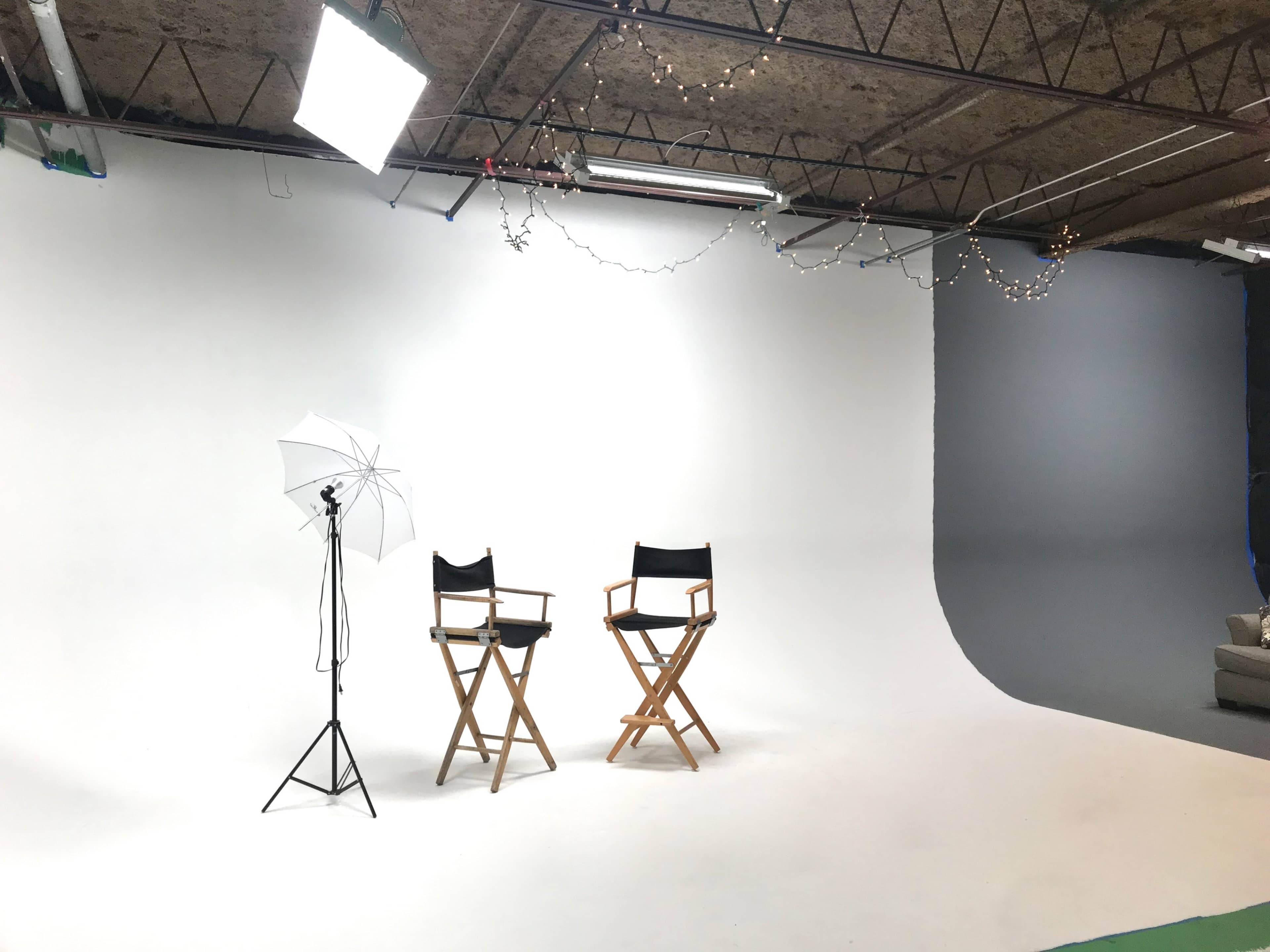 A photography studio features two director's chairs, a lighting setup, and a plain backdrop.