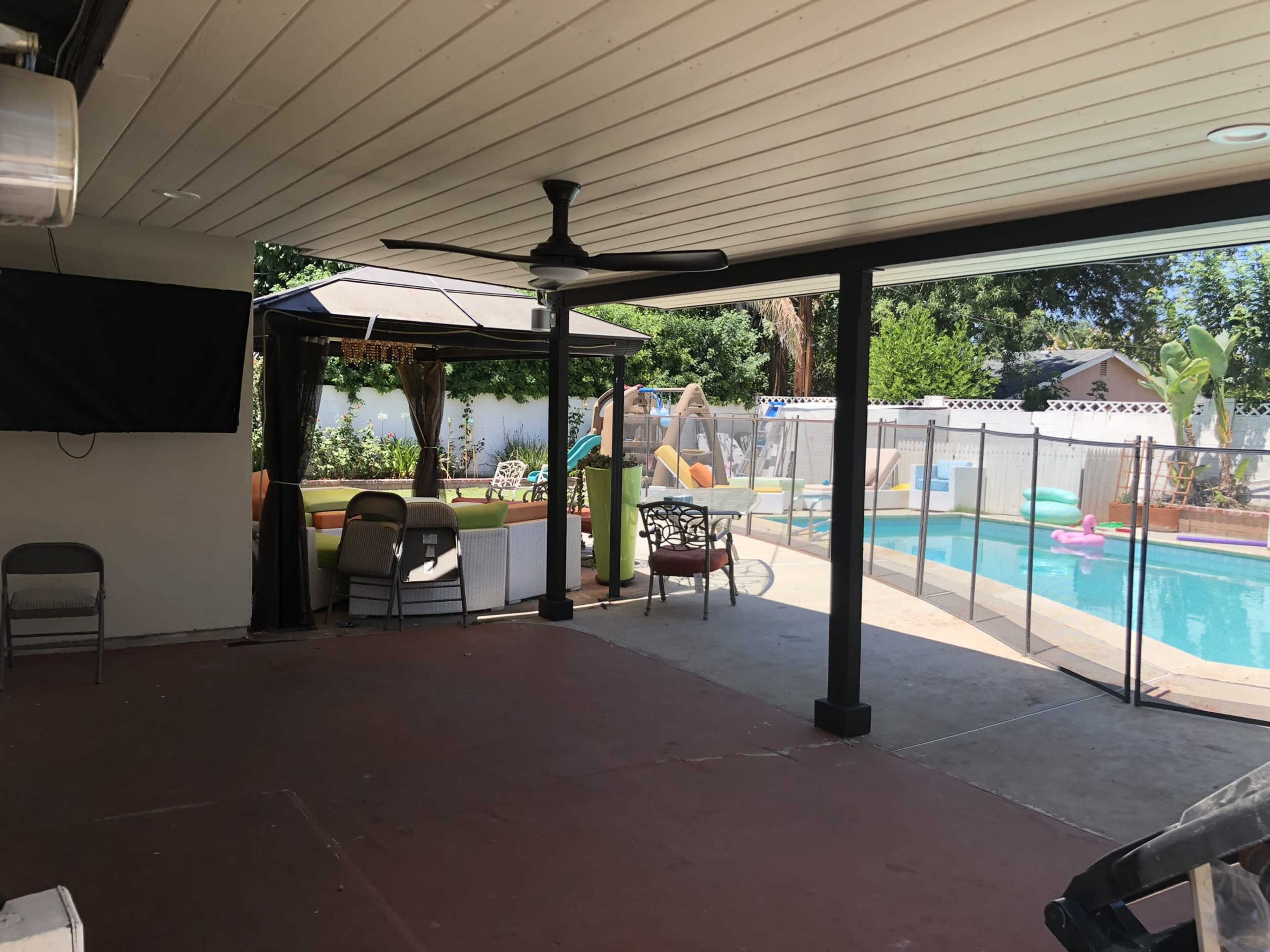 A covered patio area with a ceiling fan, leading to a swimming pool surrounded by lounge chairs and a play structure.