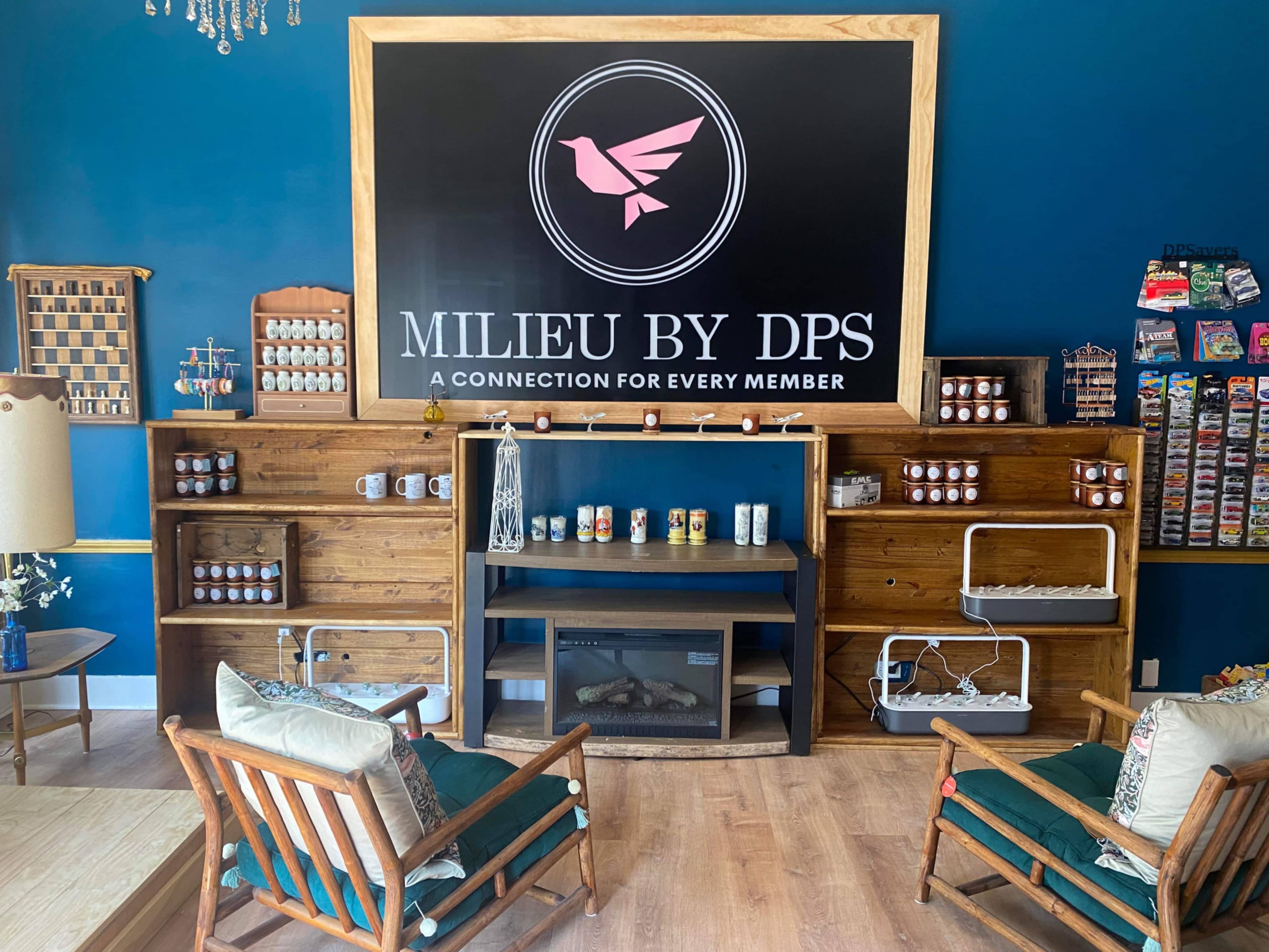 A cozy interior of a business space featuring wooden shelves, comfortable seating, and a large sign that reads "MILIEU BY DPS."