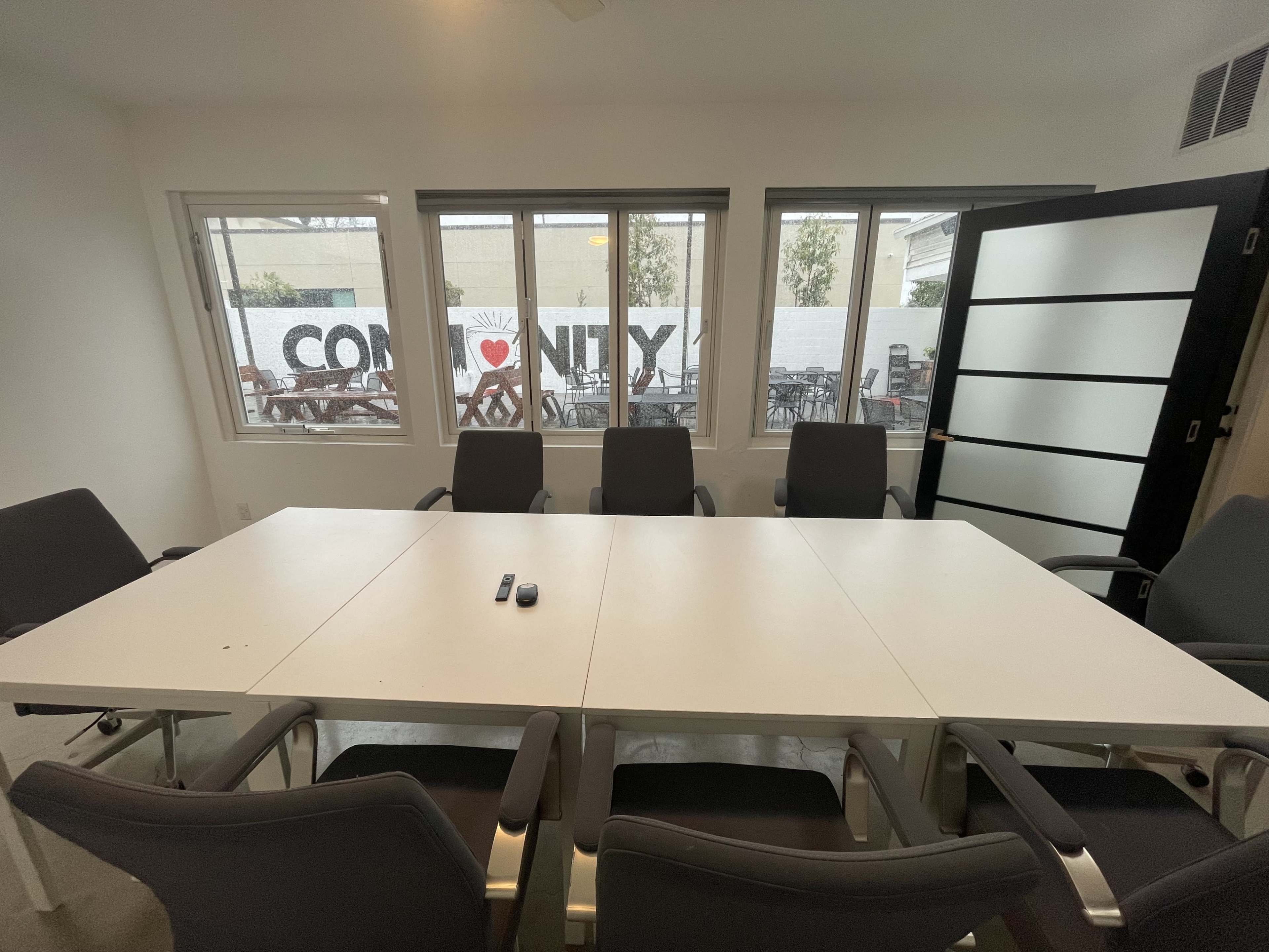 A conference room with a white table surrounded by gray chairs and large windows displaying a mural that reads "Community."