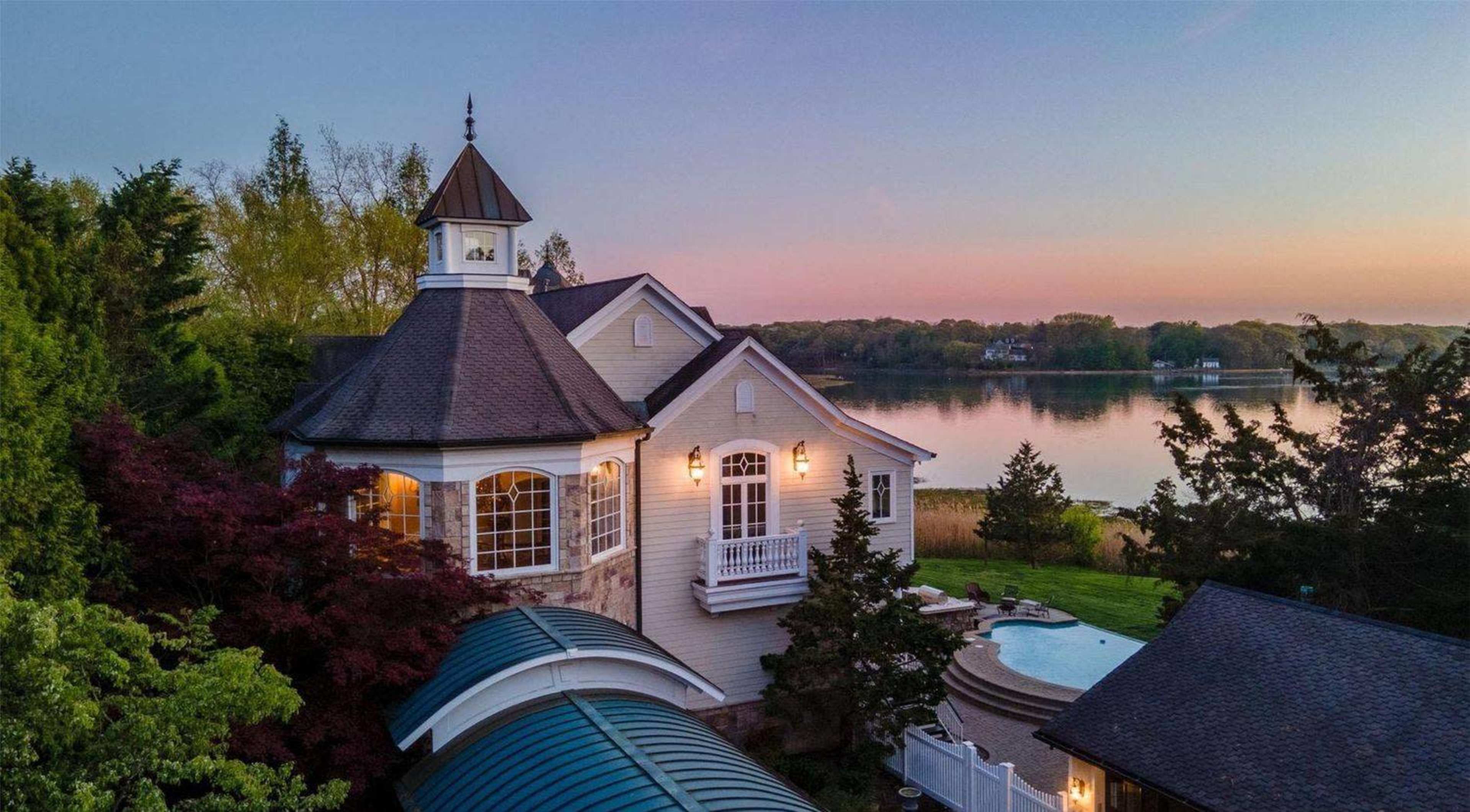 The image shows a waterfront house with a distinctive turret and surrounding trees at sunset.