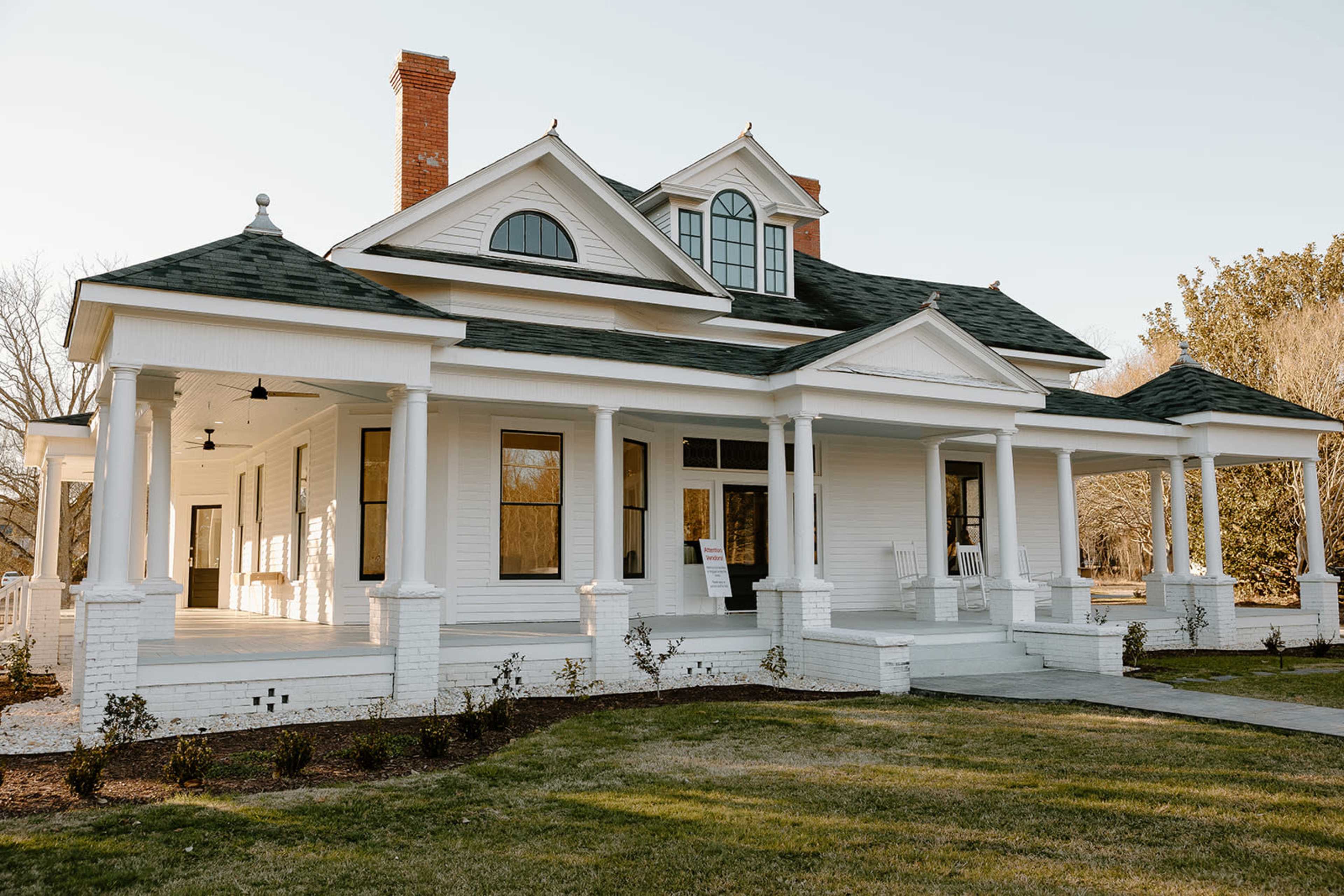 A large white house with a steep roof, multiple columns on the front porch, and a manicured lawn.