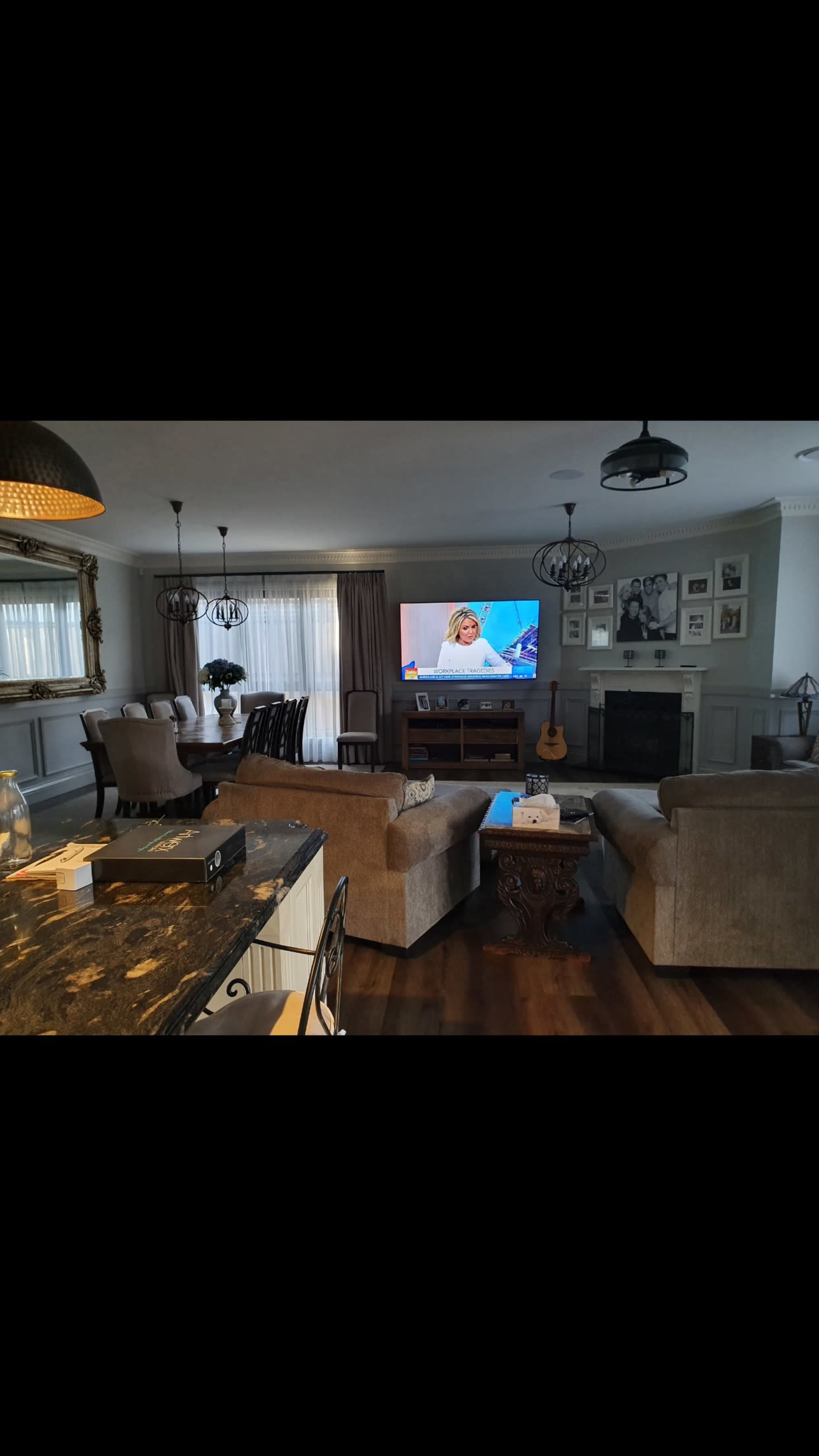 A neatly arranged living room features two sofas facing a large television, with a kitchen bar visible in the foreground.
