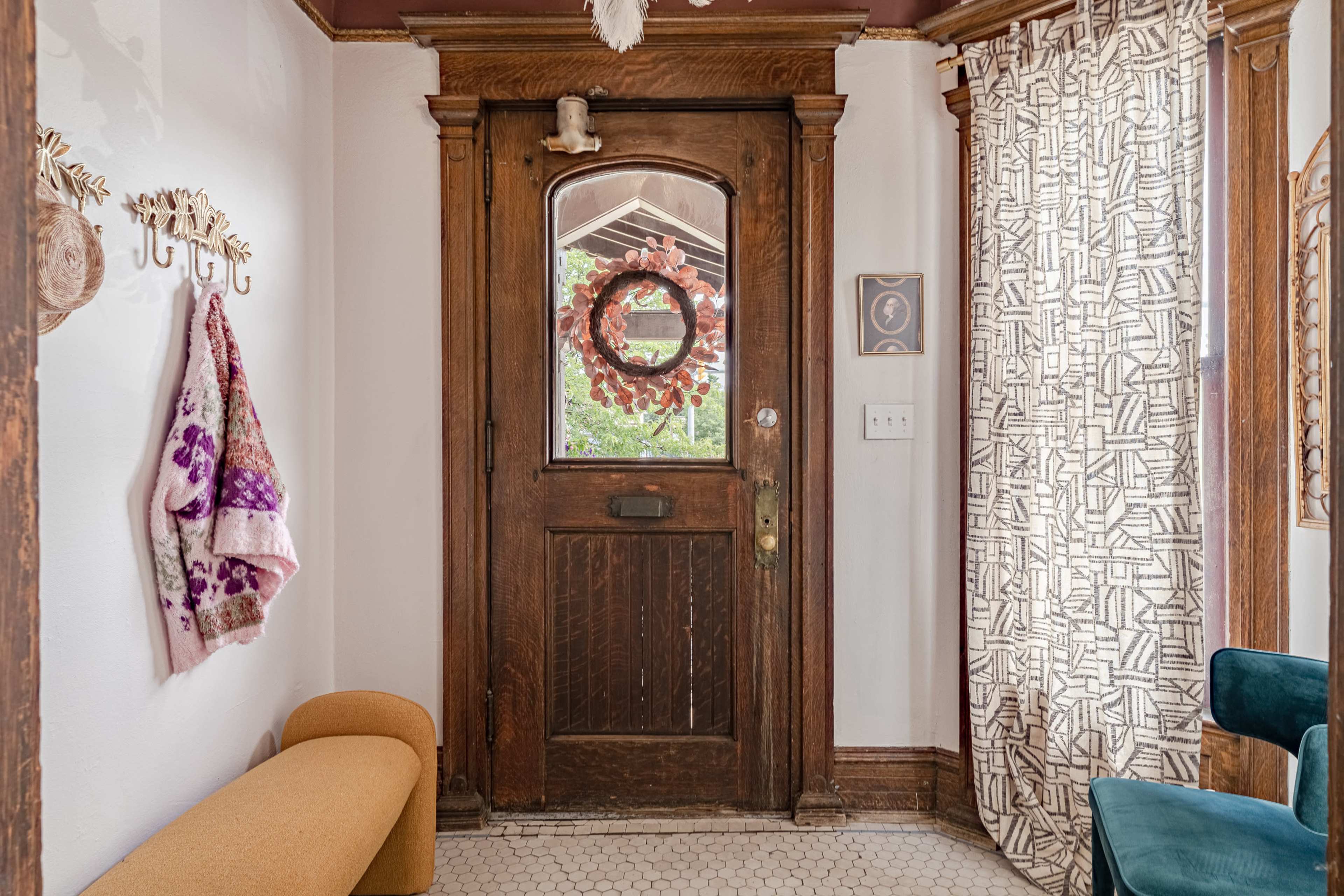 An entryway featuring a wooden door with a wreath, a decorative curtain, and a bench with hooks for hanging accessories.
