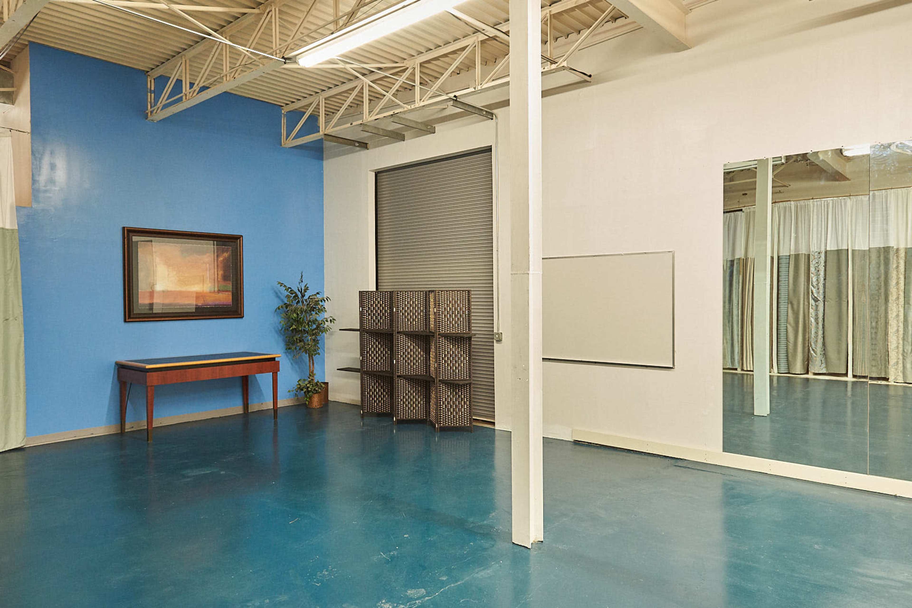 A spacious interior with a blue wall, a wooden table, a decorative plant, a folding screen, and a large mirror.
