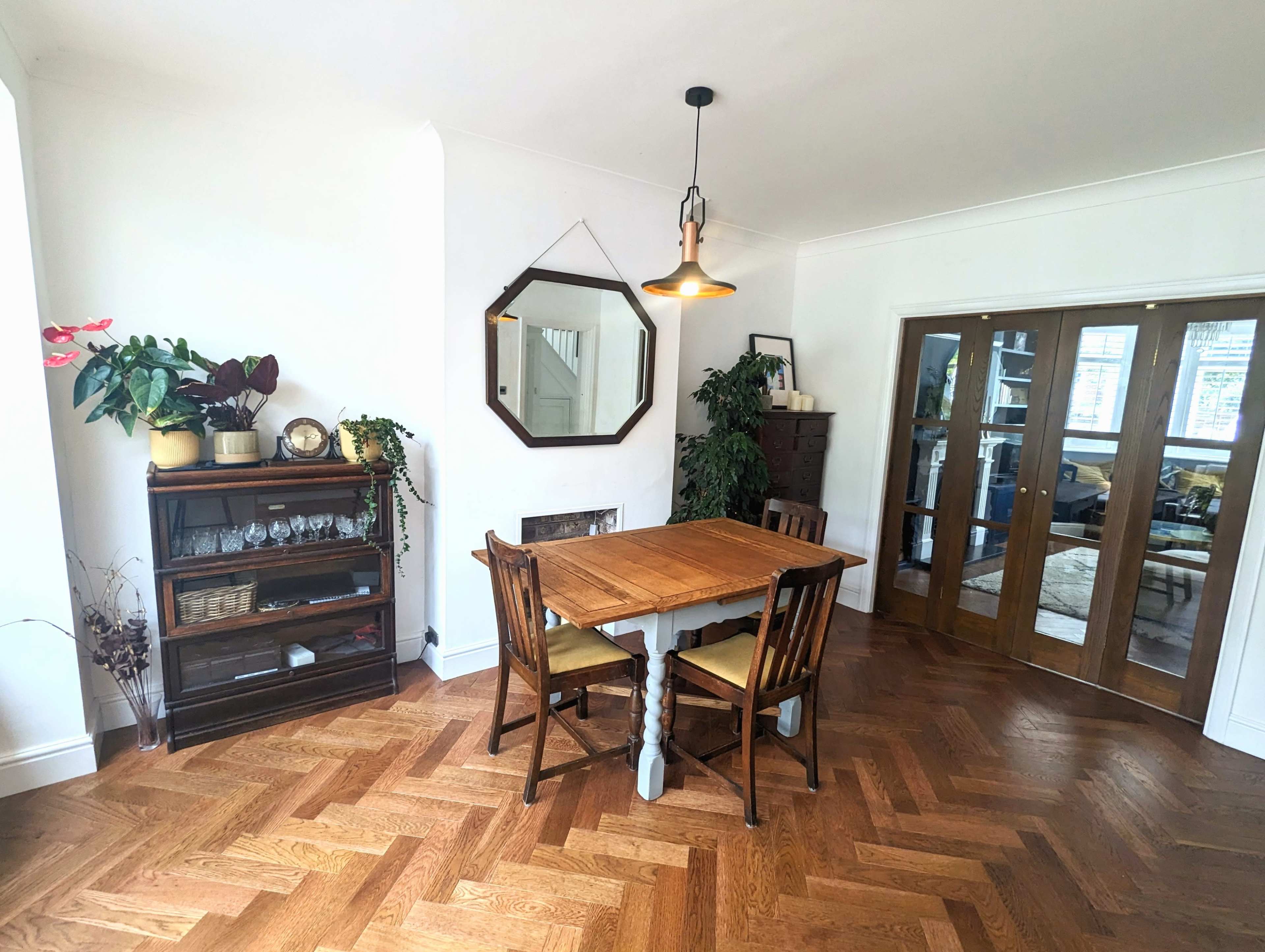 A dining area featuring a wooden table with two chairs, a storage unit on the left, and a large mirror hanging on the wall.