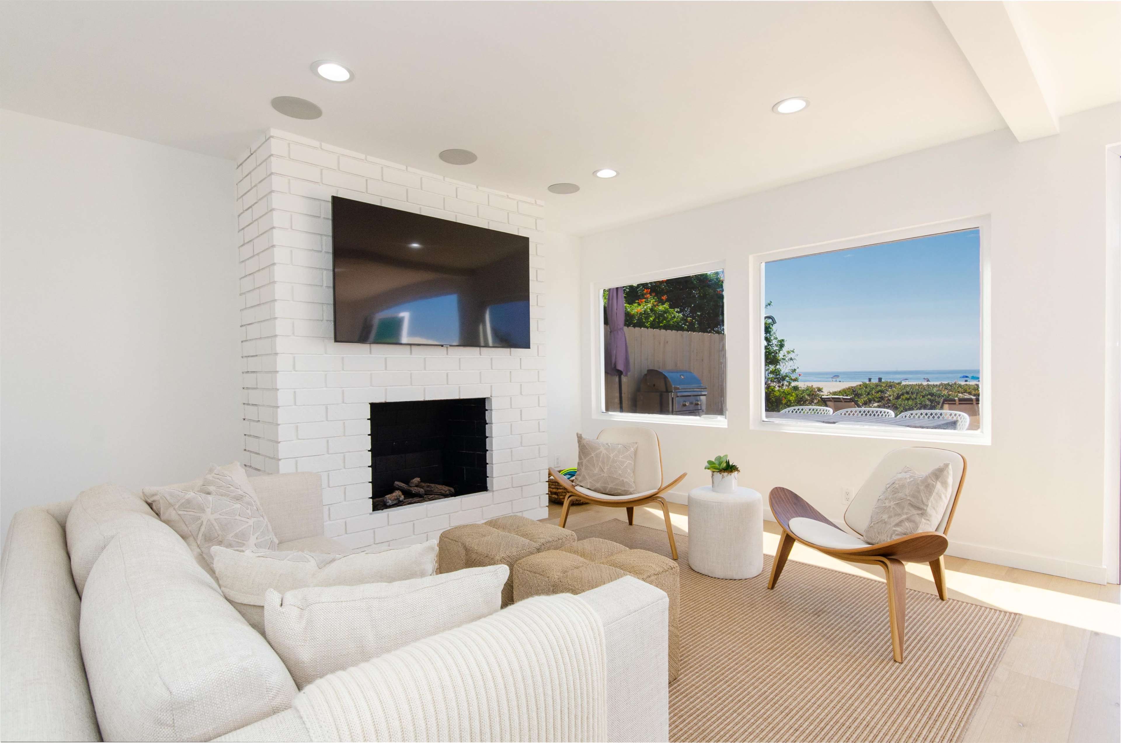 A modern living room features a white brick fireplace, a mounted television, and large windows overlooking a coastal view.