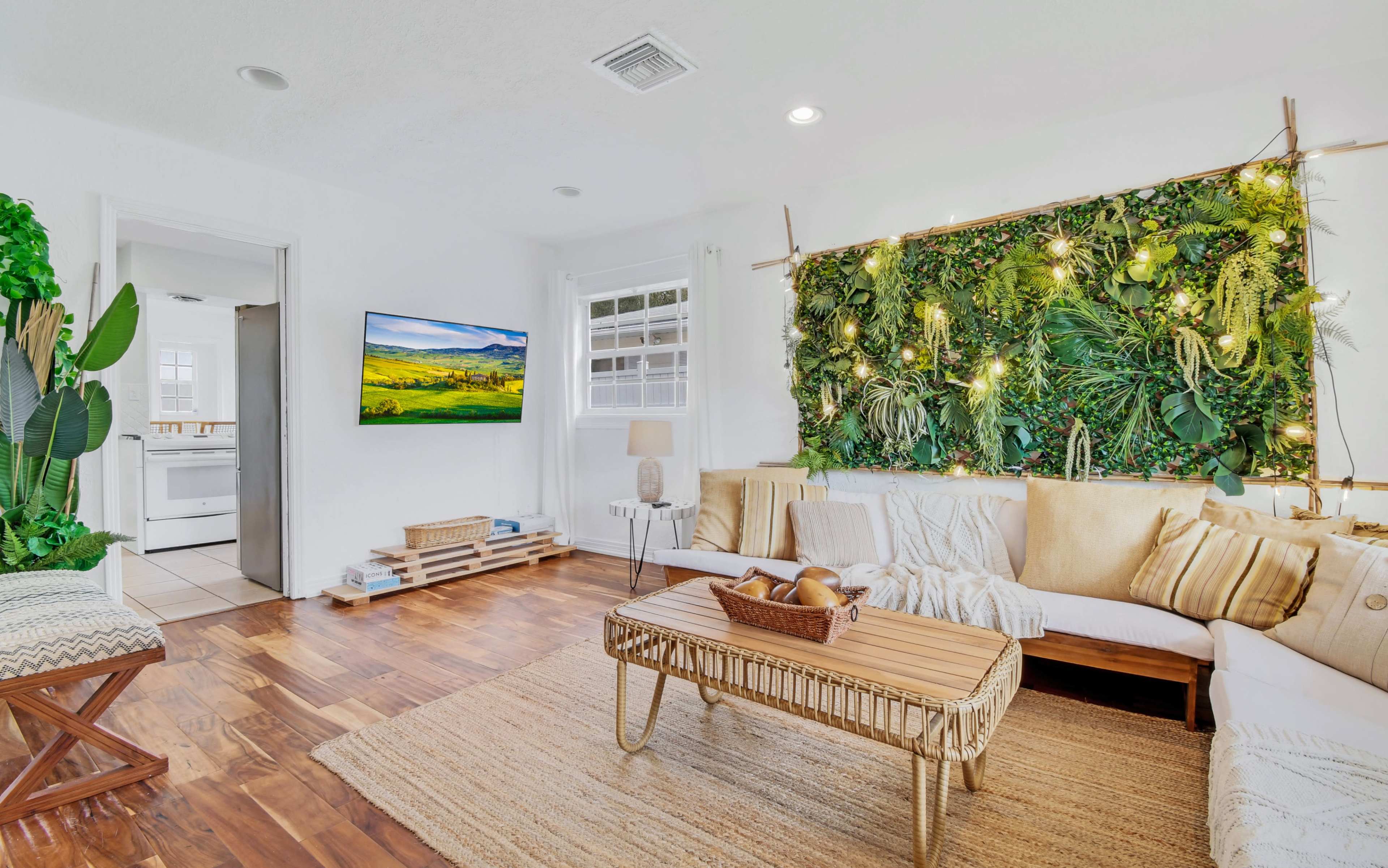 The living room features a sectional sofa, a wooden coffee table, a large television on the wall, and a vertical garden adorned with lights.