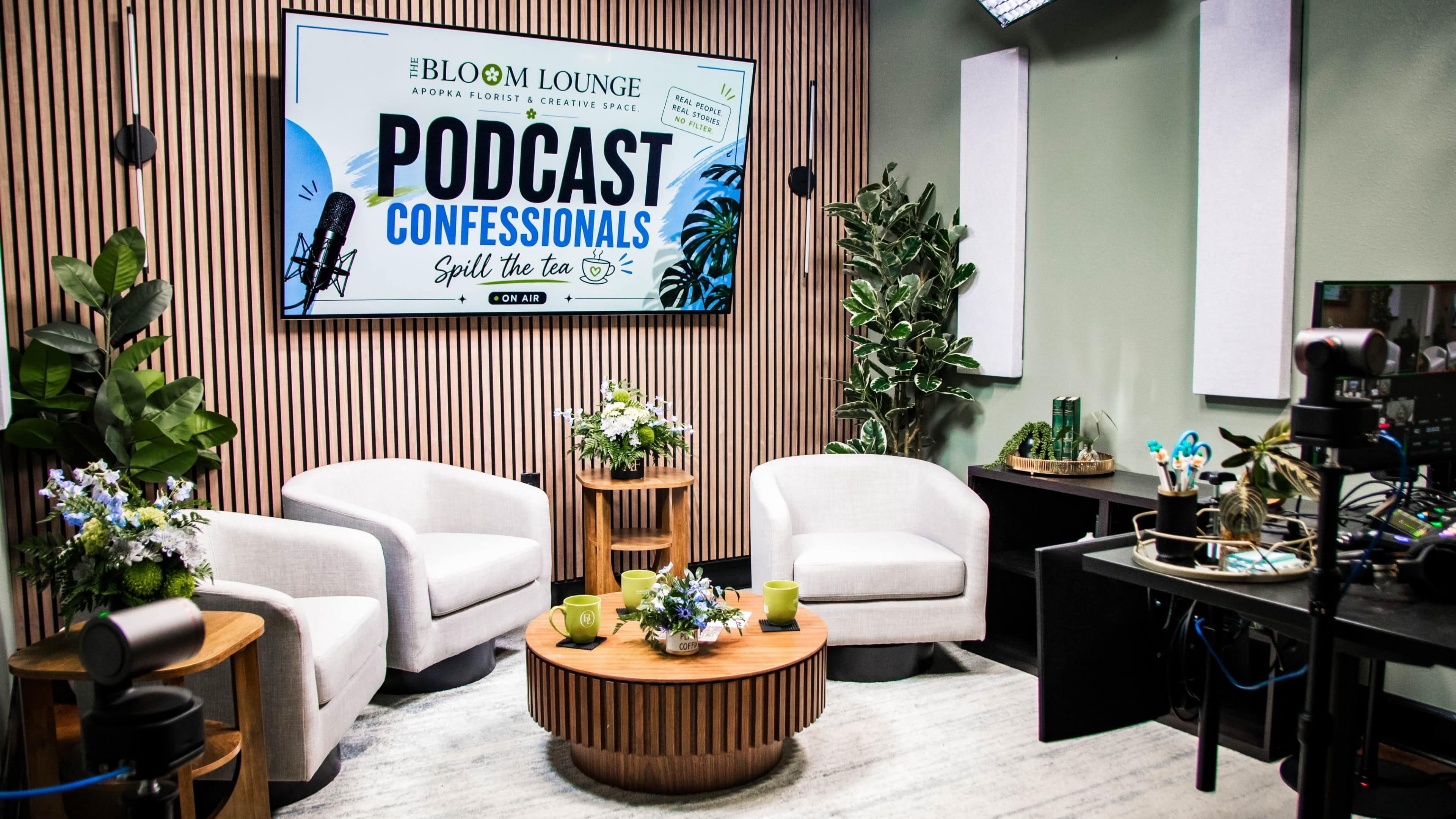 The image features a podcast recording studio with three white chairs arranged around a wooden table, surrounded by greenery and a large screen displaying the text "PODCAST CONFESSIONALS."