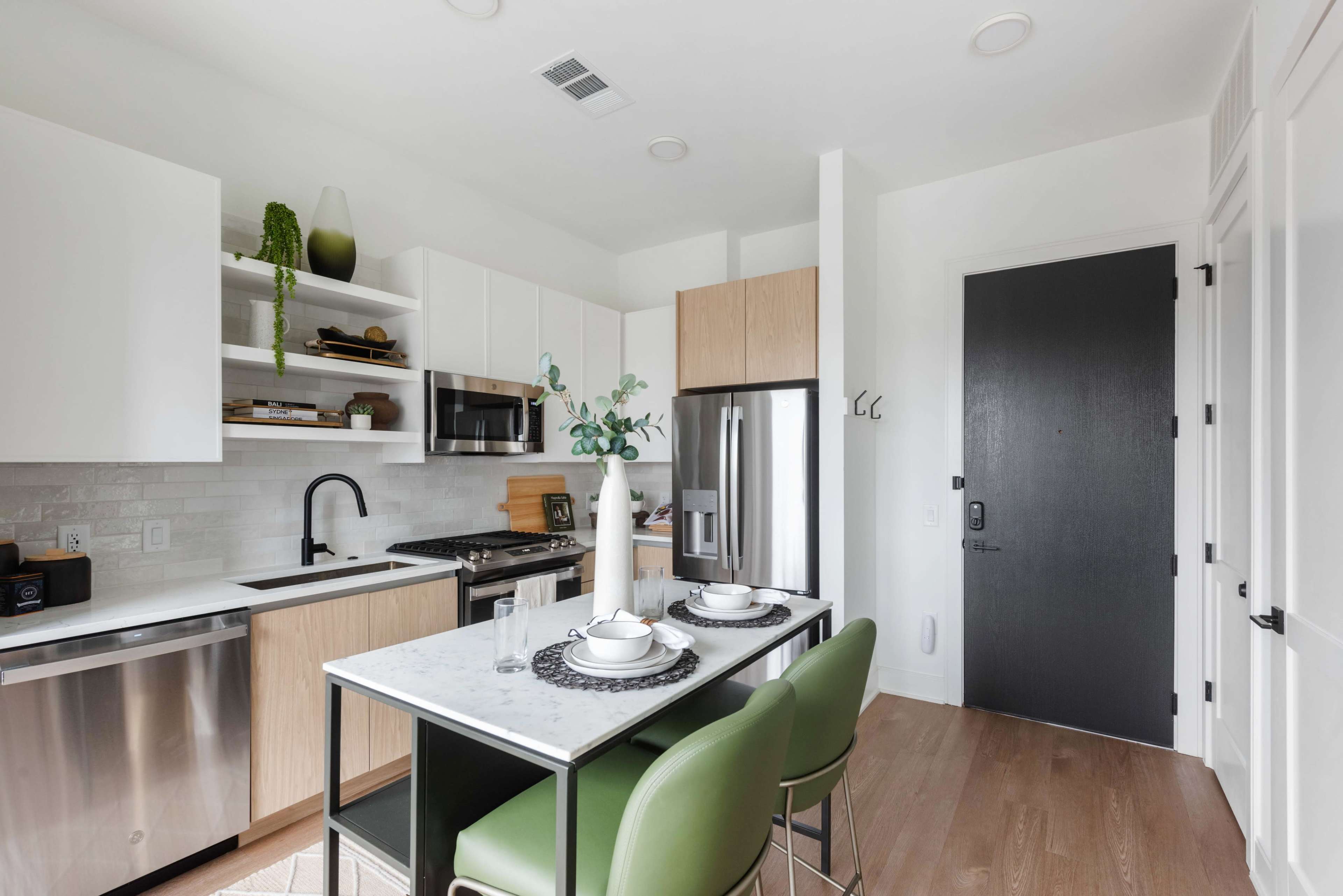 The image shows a modern kitchen with a marble dining table set for two, stainless steel appliances, and light wood cabinetry.