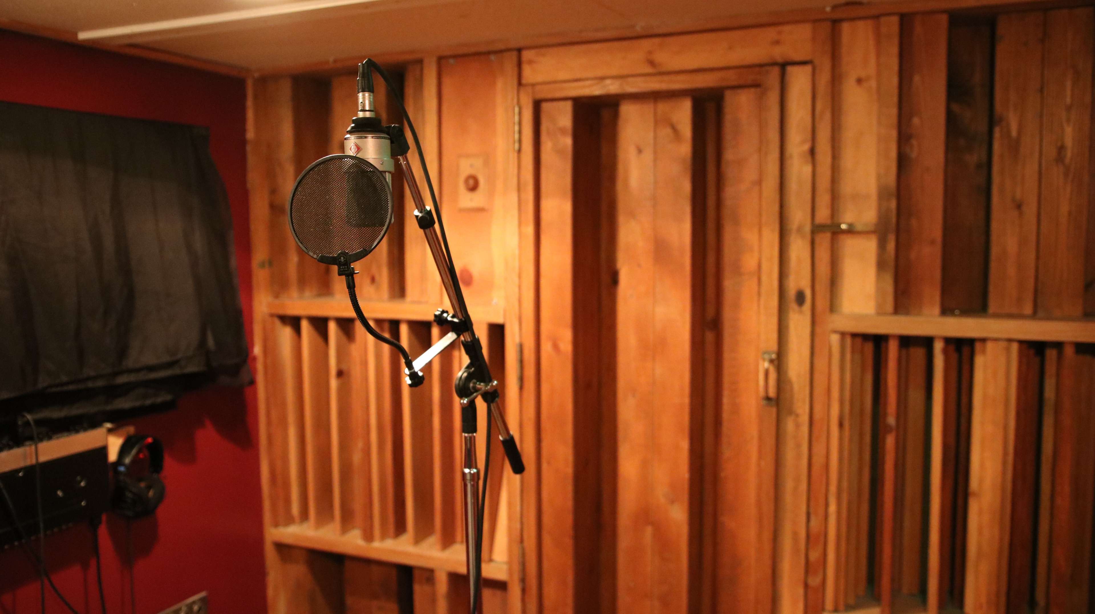 A microphone on a stand is positioned in a wooden sound booth with black curtains and a closed door.