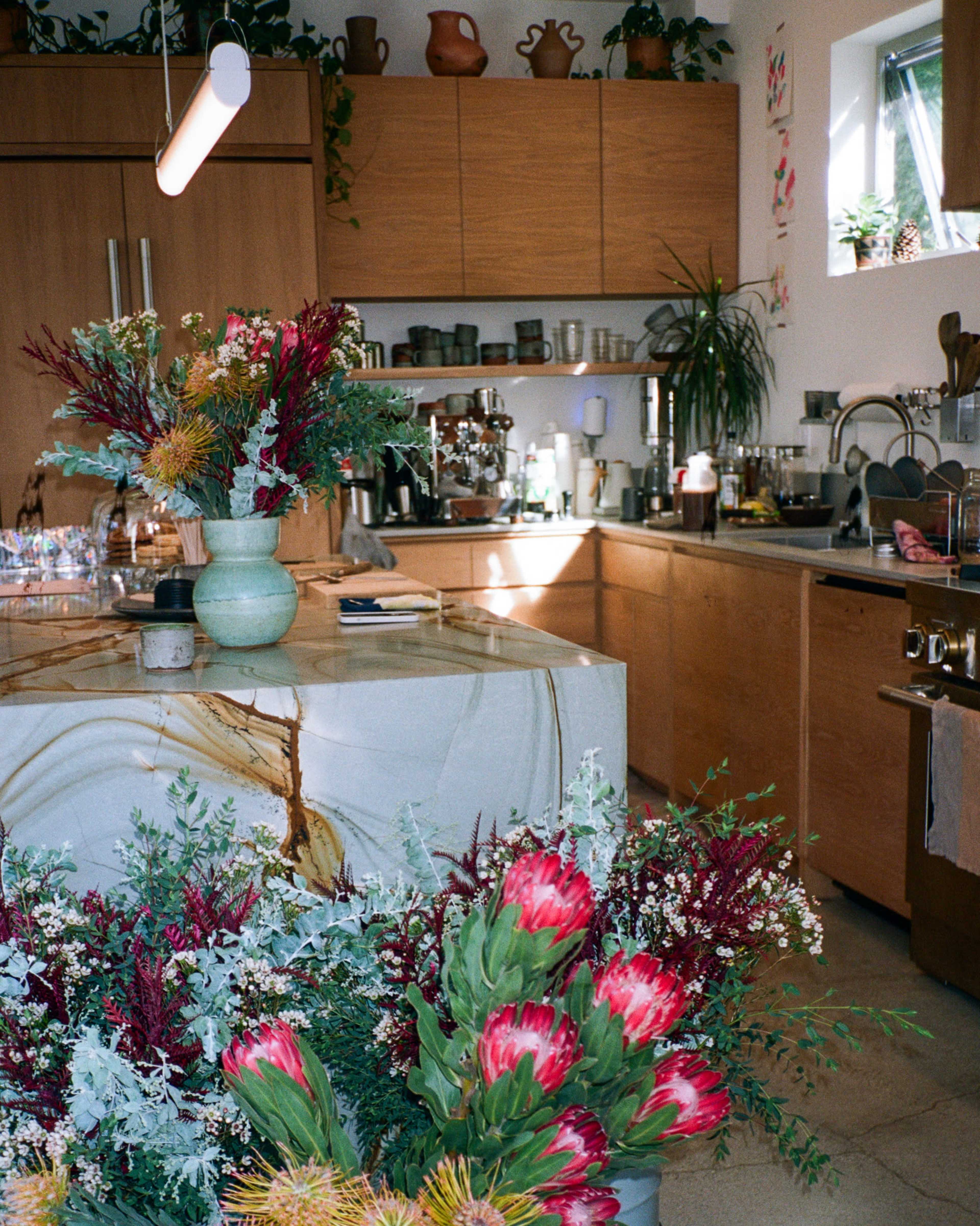 A kitchen features a large island with a decorative vase of flowers and a backdrop of wooden cabinetry and countertops.