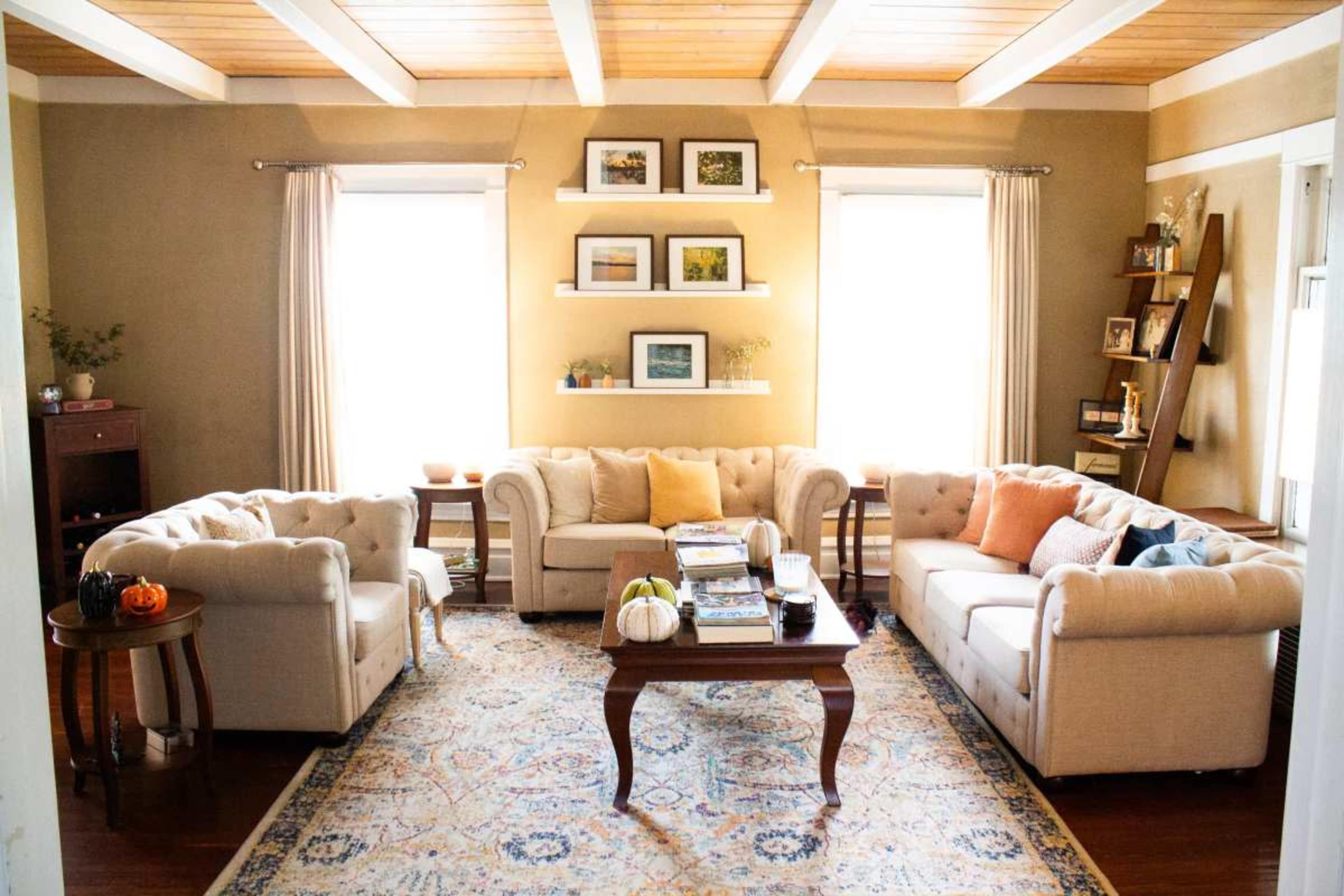 A cozy living room with beige sofas arranged around a wooden table, adorned with decorative items, and framed pictures on the walls.