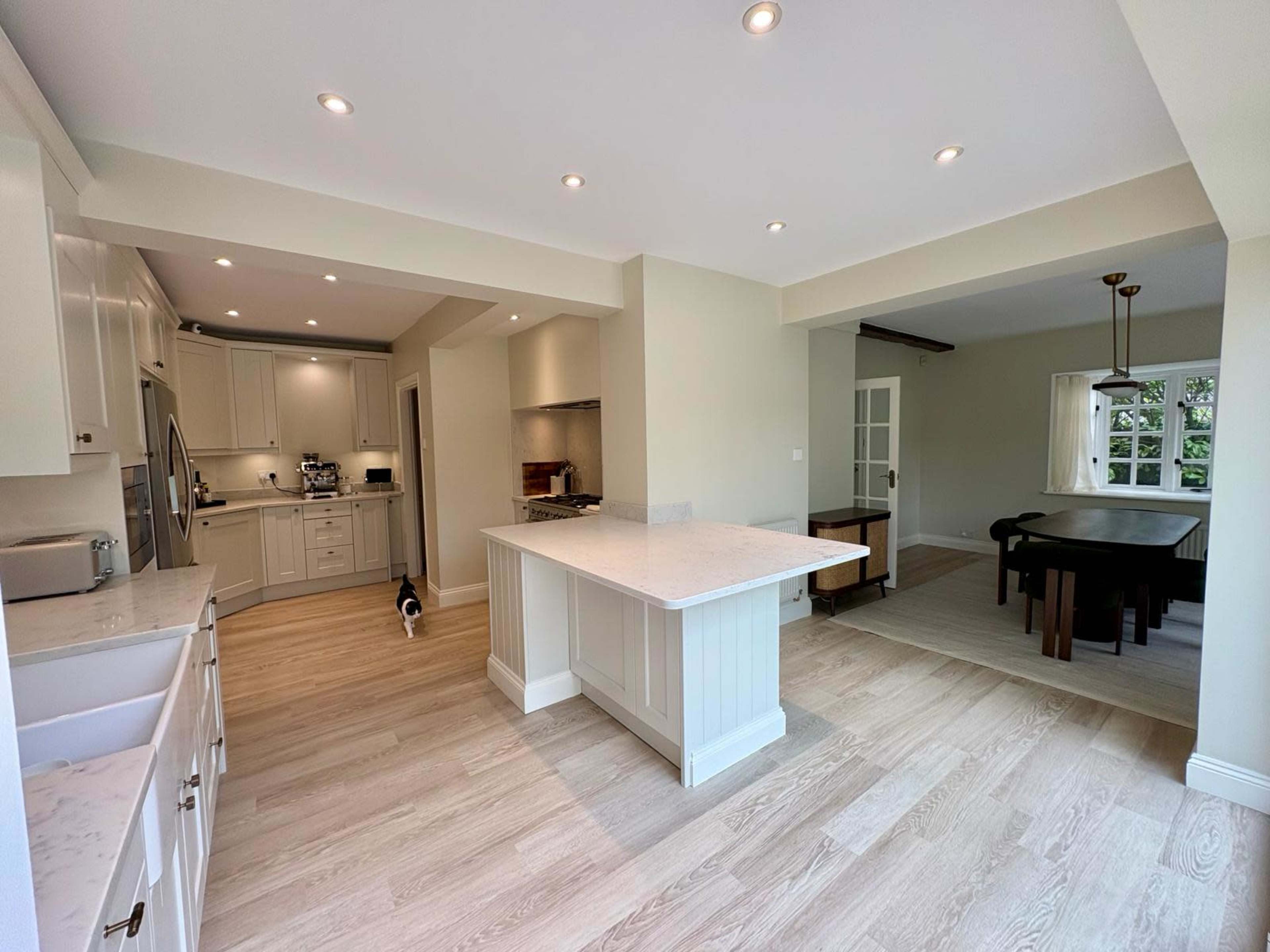 The image shows a modern kitchen with white cabinets, an island, and a dining area featuring a wooden table and chairs.