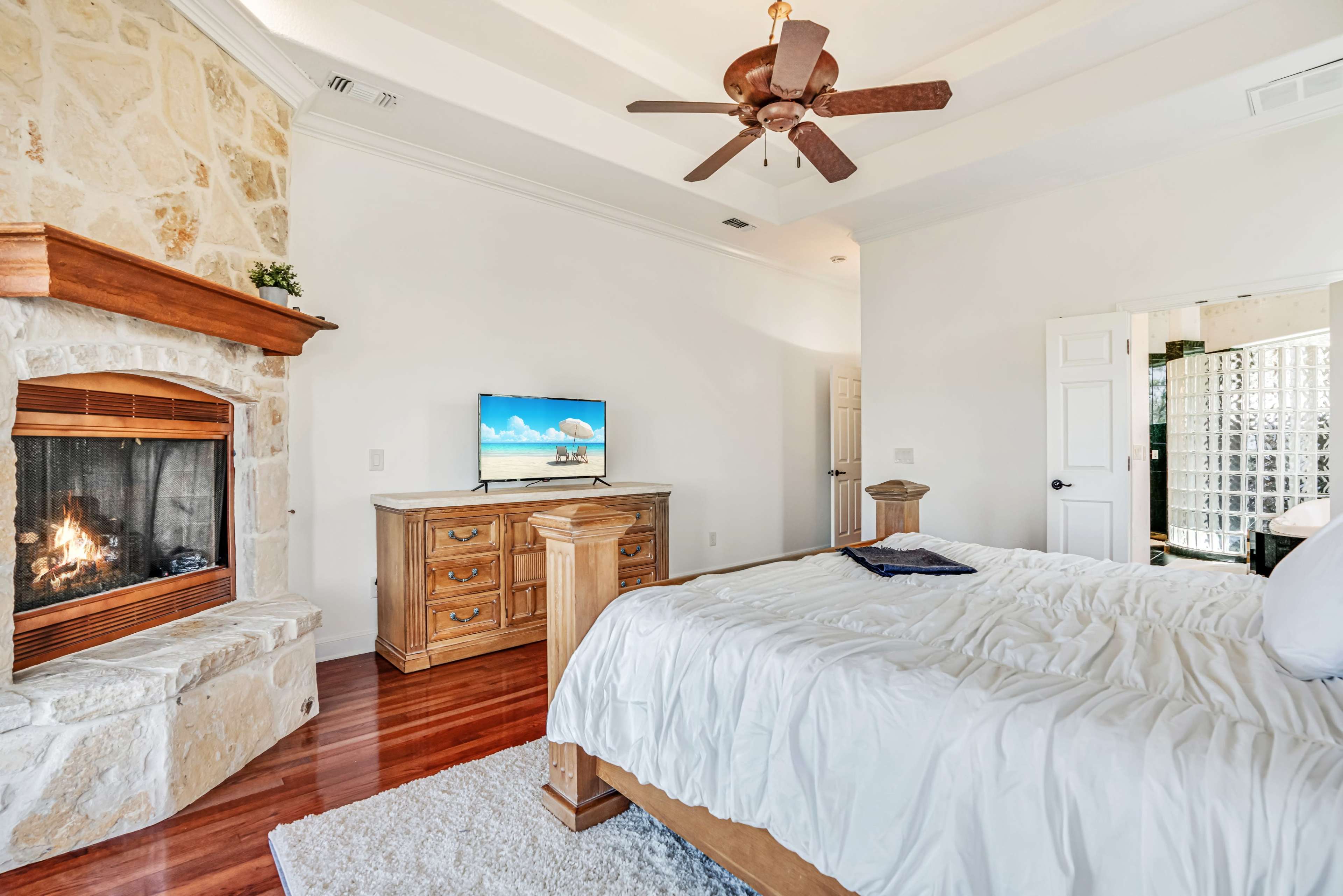 A spacious bedroom featuring a wooden bed, a firewood fireplace with a stone facade, and a television mounted on the wall.