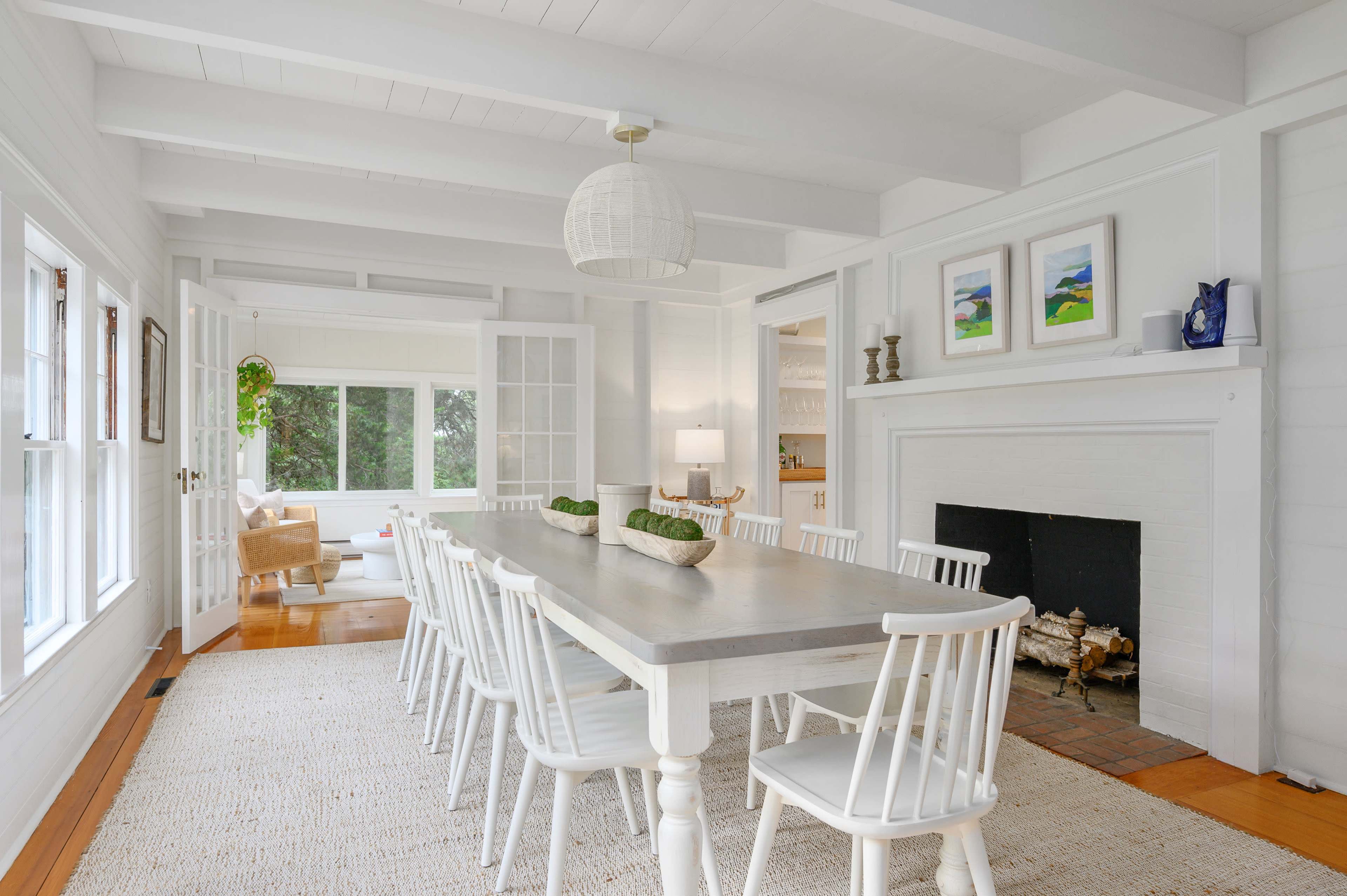 A bright, airy dining room with a long table, white chairs, and large windows that allow natural light to fill the space.