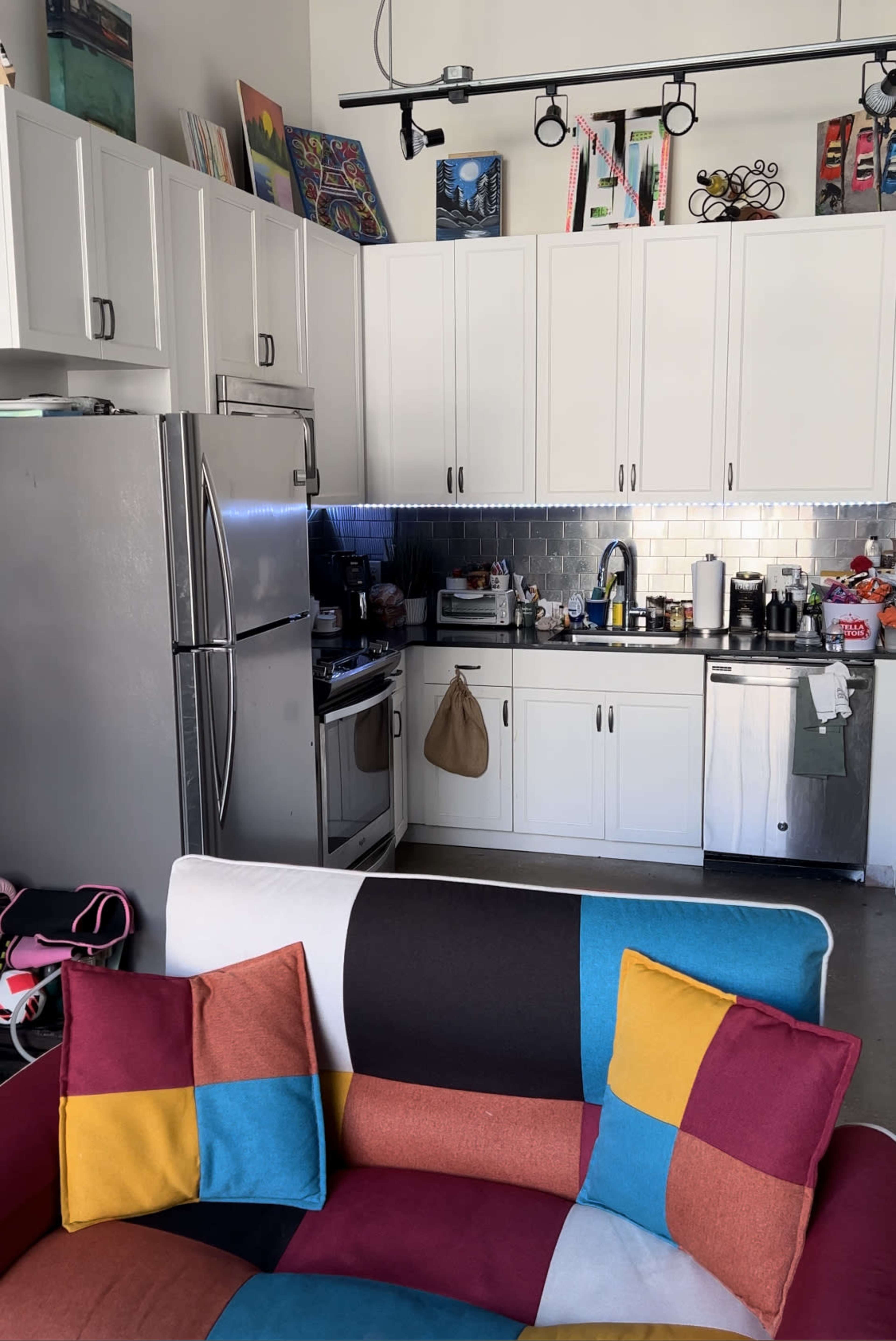A colorful couch sits in front of a modern kitchen with stainless steel appliances and white cabinets.