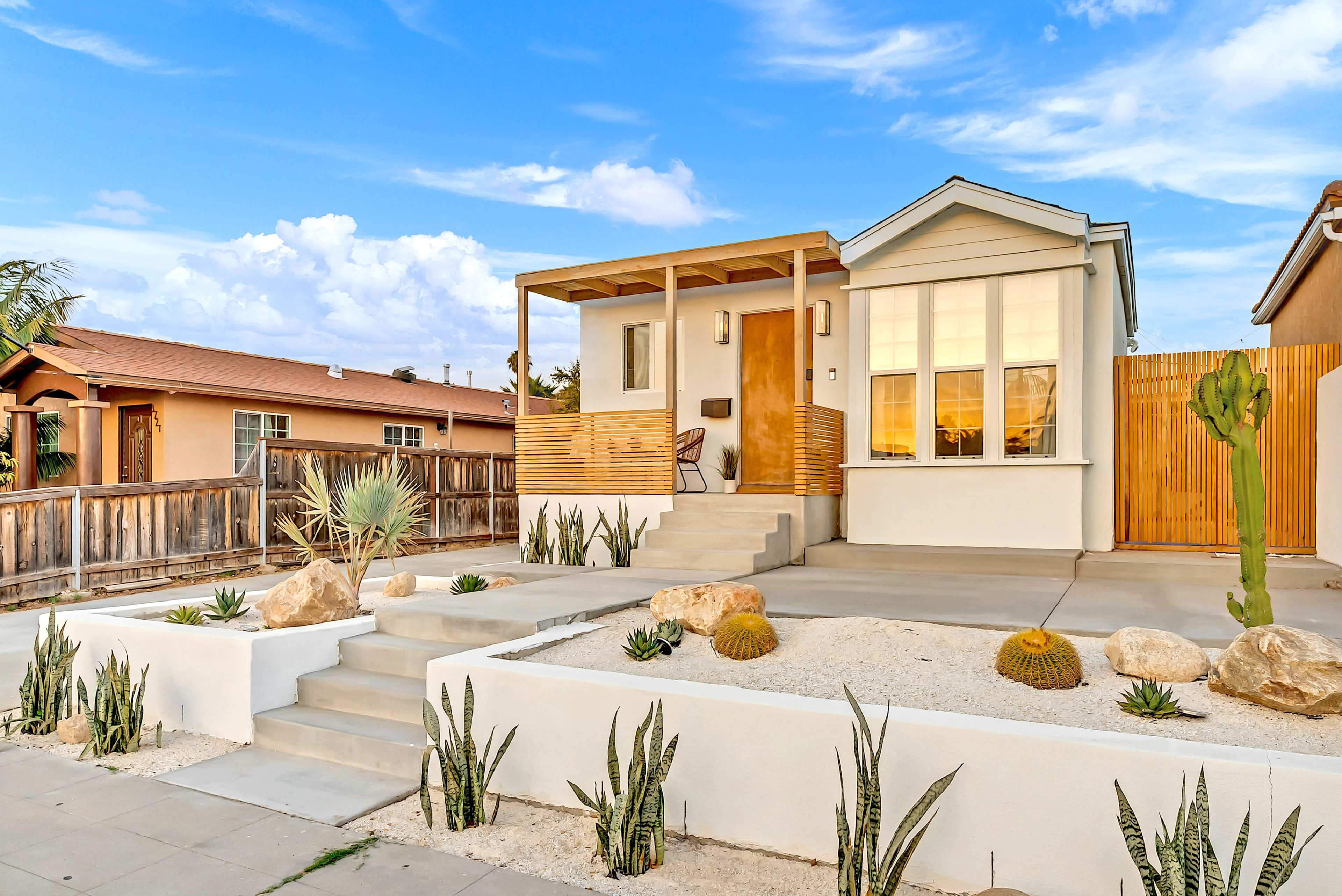 A modern single-story house with a front porch, surrounded by a landscaped yard featuring cacti, rocks, and gravel.