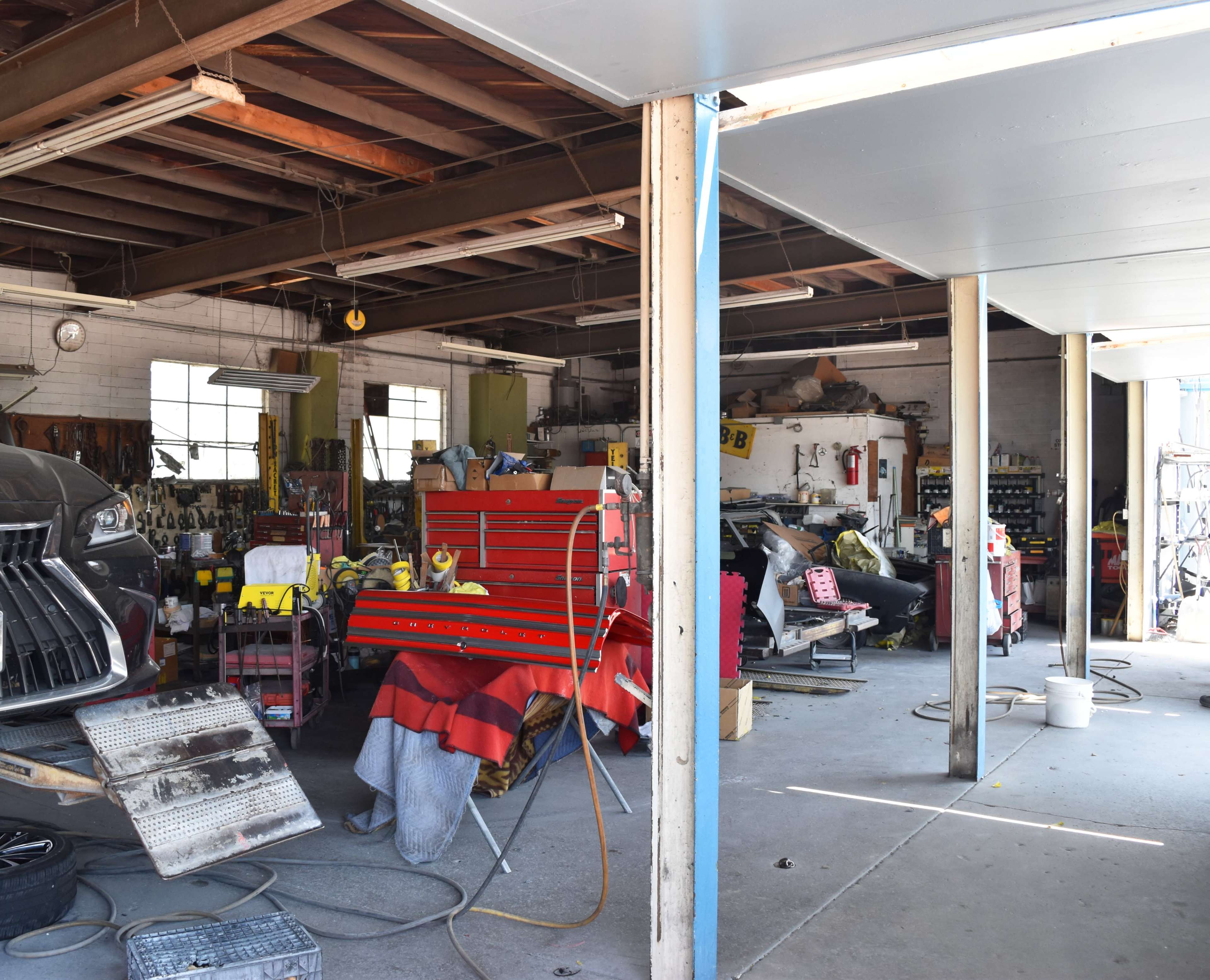 The image shows a cluttered garage workspace with tools, car parts, and equipment visible throughout the area.