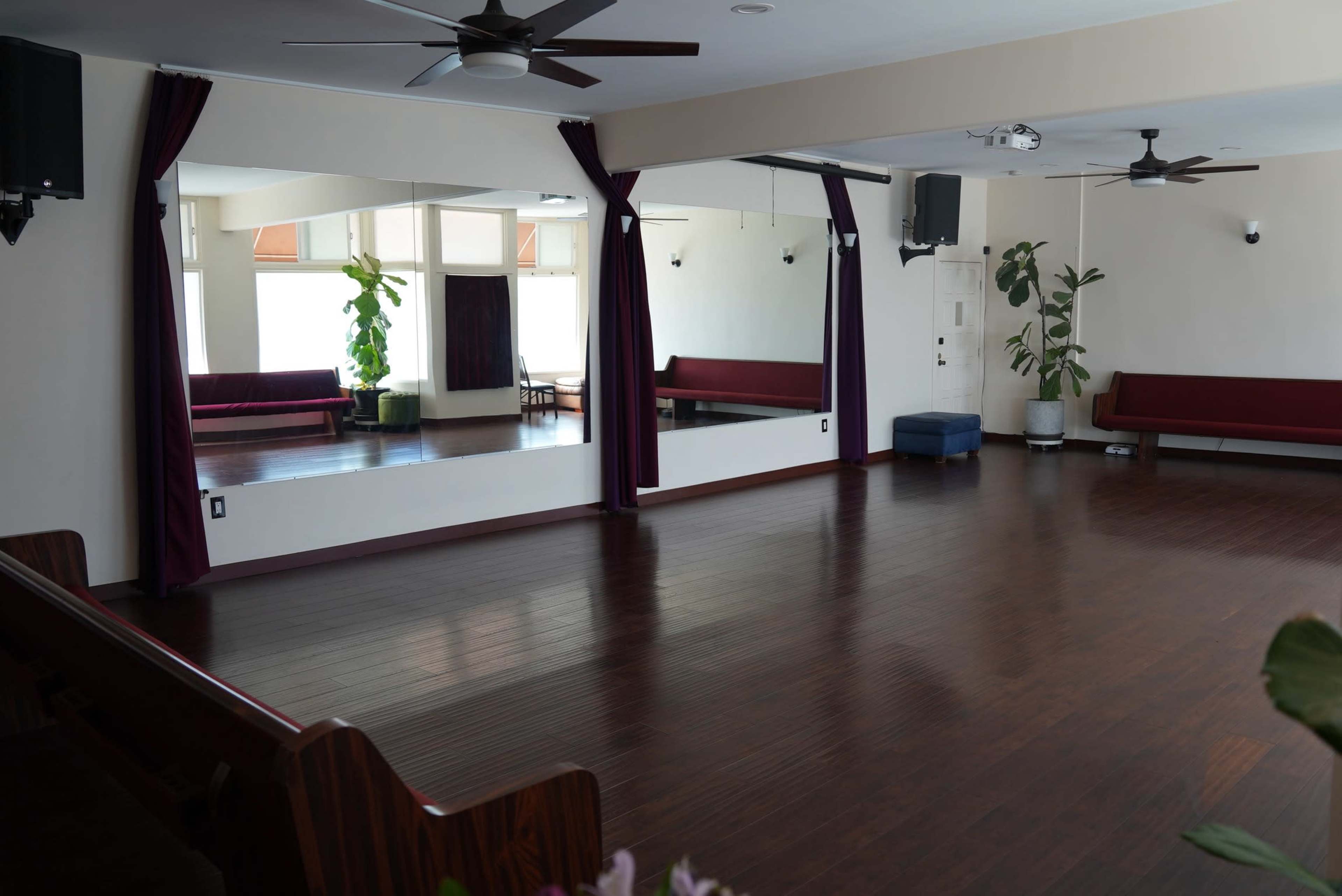 A spacious dance studio with wooden flooring, large mirrors on the walls, and seating along two sides.
