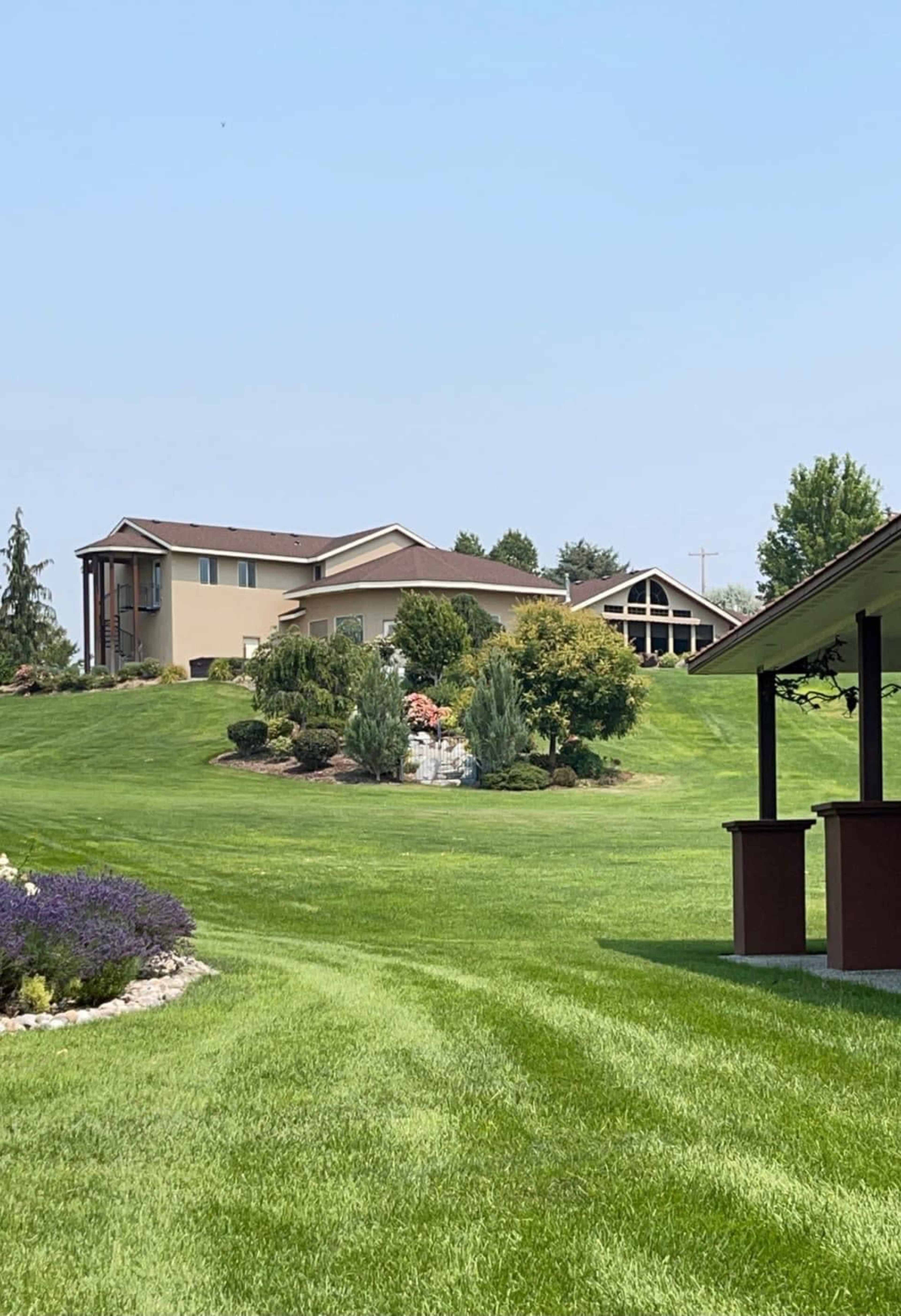 A spacious green lawn slopes gently towards a multi-level house with large windows and landscaped gardens in the background.