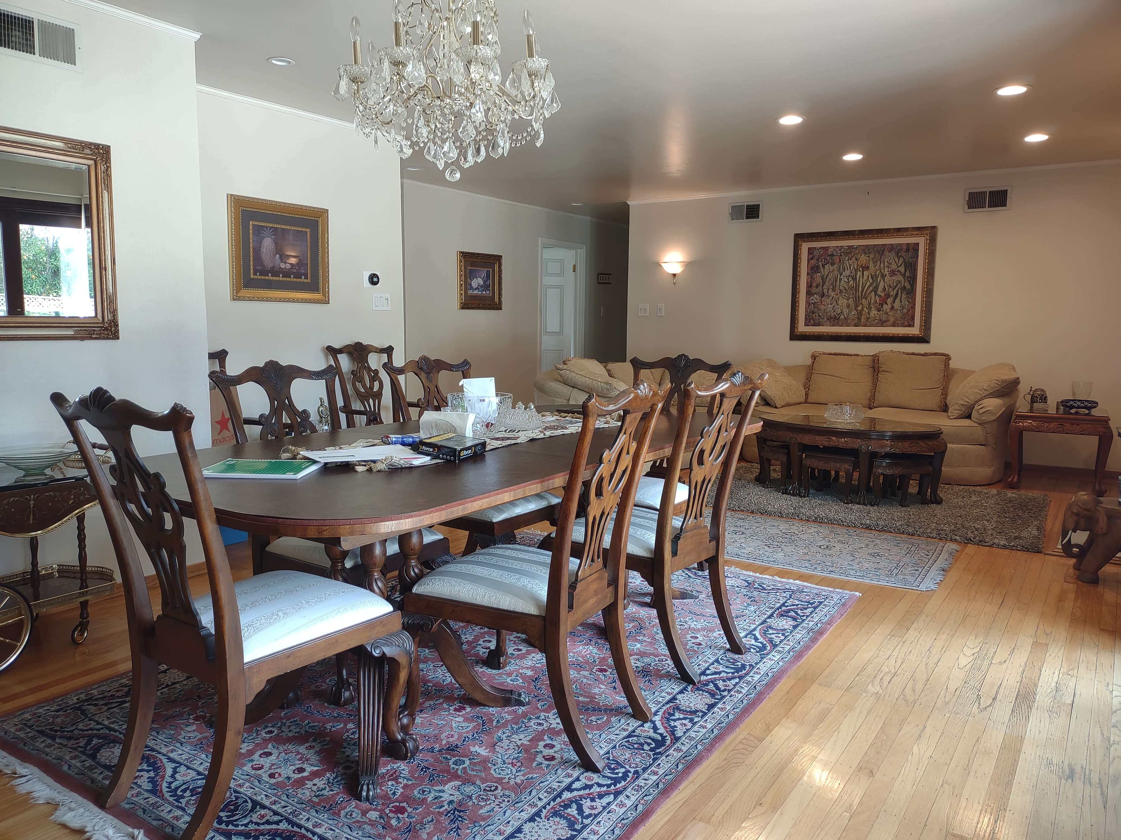 A spacious dining room featuring a large wooden table surrounded by ornate chairs, a chandelier overhead, and a comfortable seating area in the background.