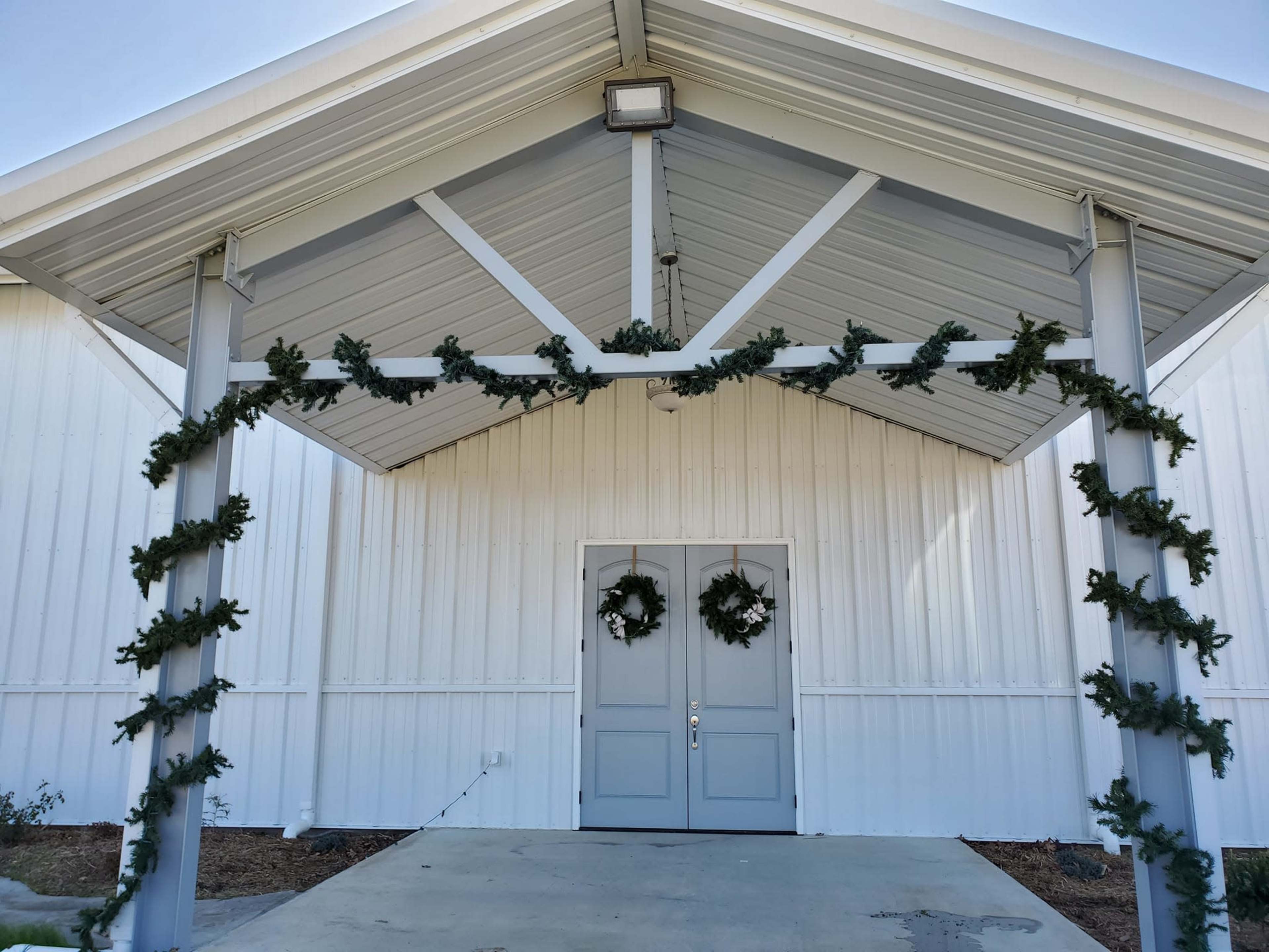 A covered entrance to a building with two wreaths hanging on the doors and garland draped along the overhang.
