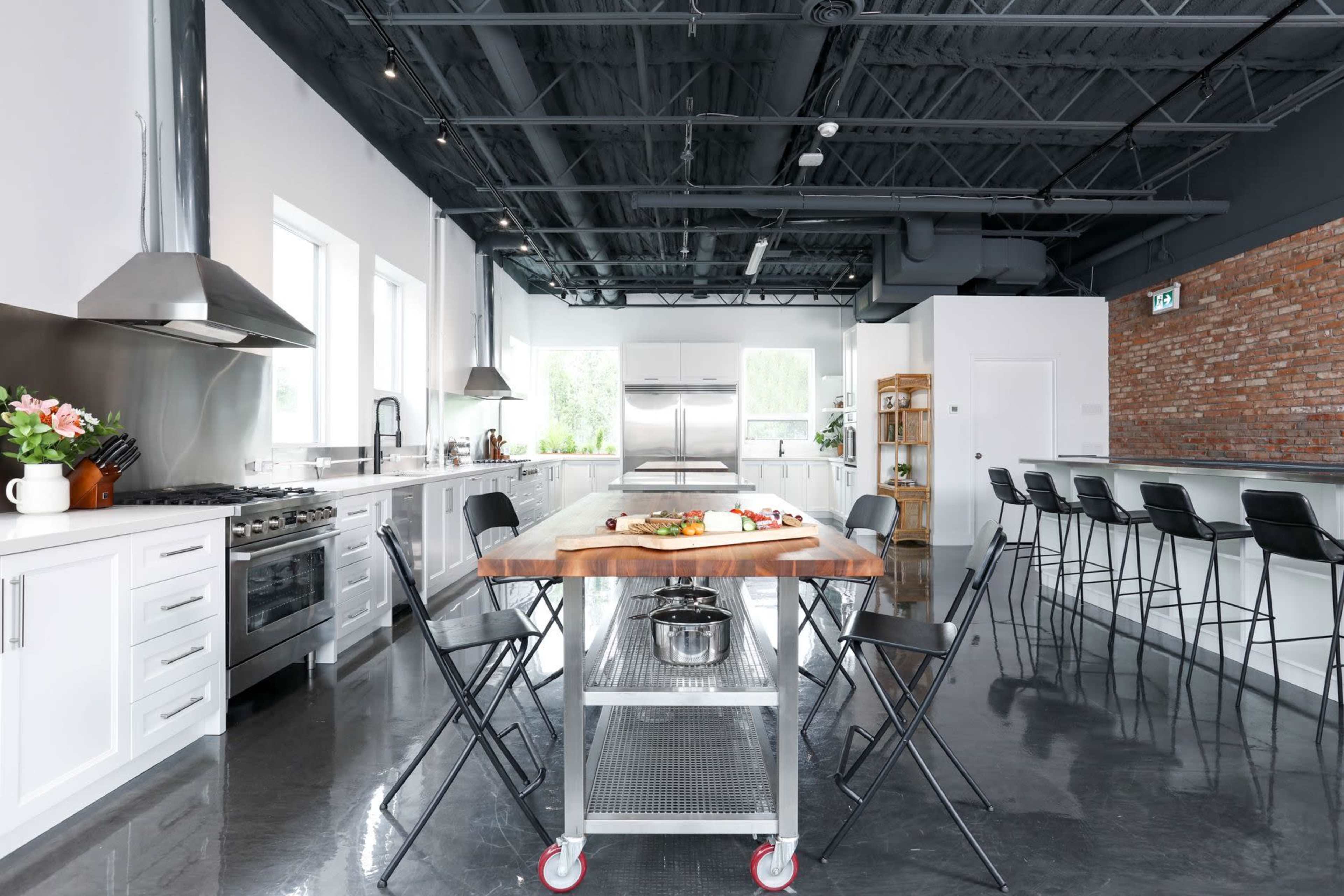 A spacious kitchen features a large wooden island in the center, flanked by metal stools and equipped with modern appliances and white cabinetry.