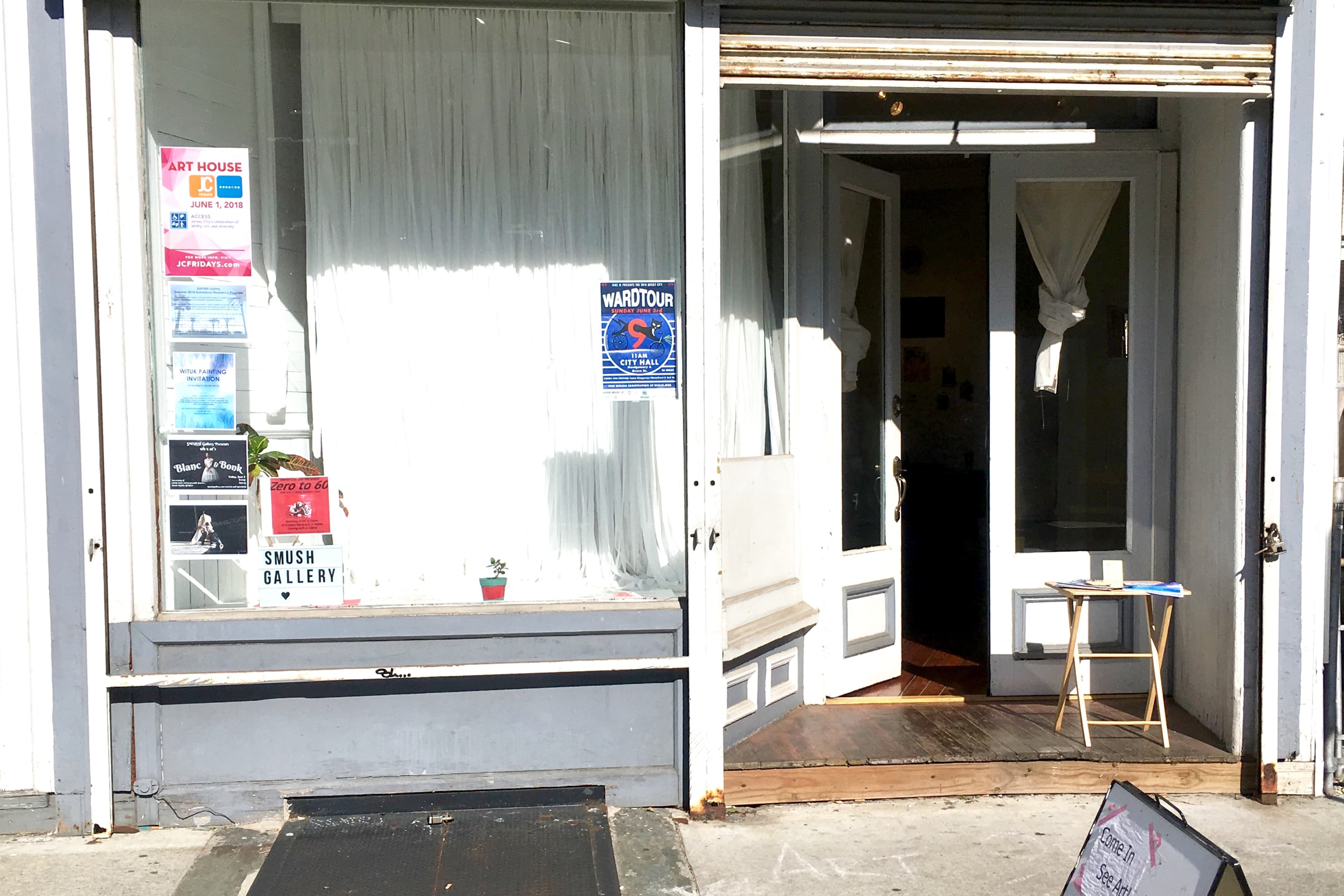 The storefront features a glass door with a white curtain behind it, displaying various posters and signs, including one for an art gallery.