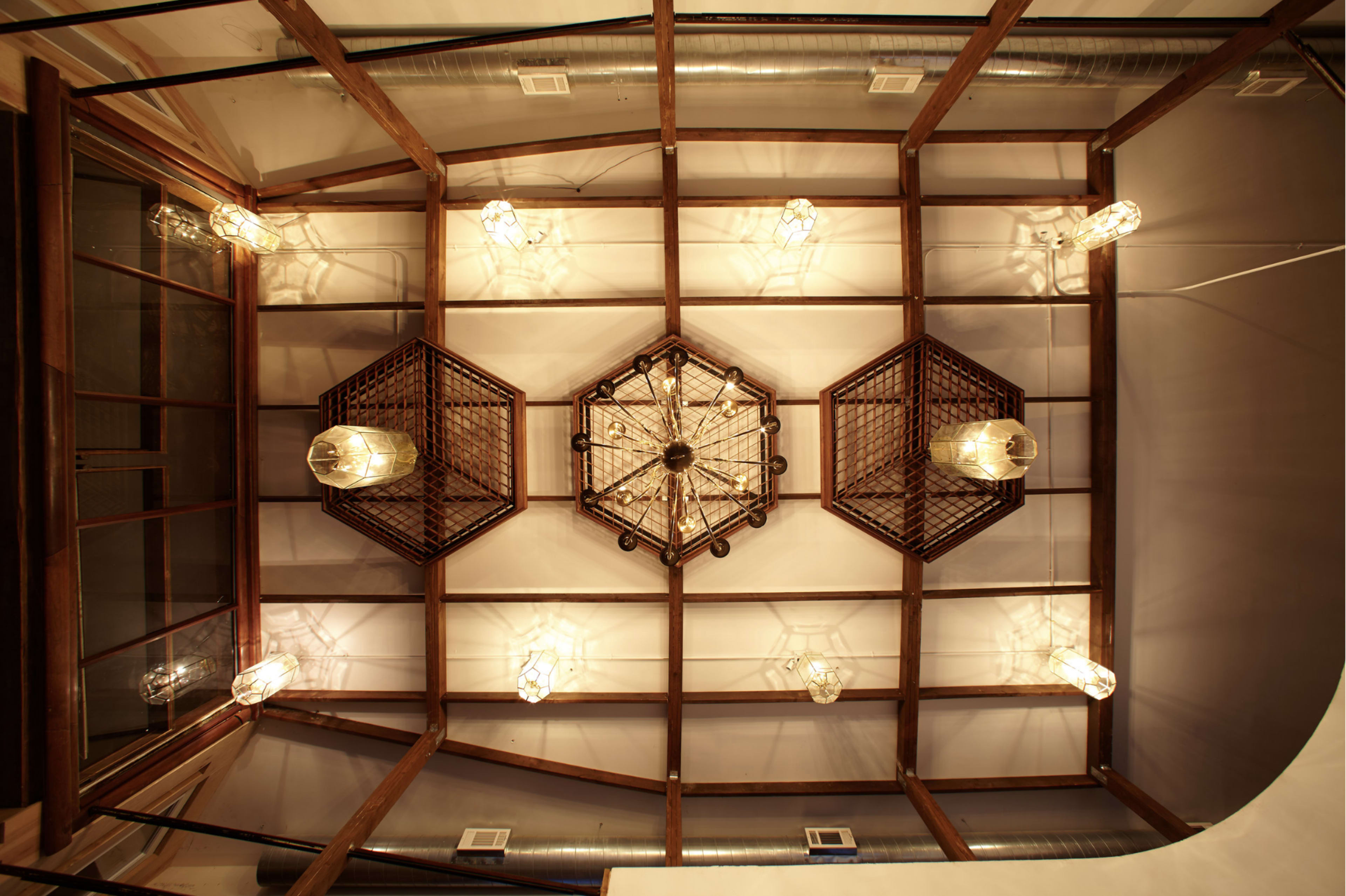A ceiling with wooden beams, a central circular chandelier, and several hanging light fixtures arranged symmetrically.
