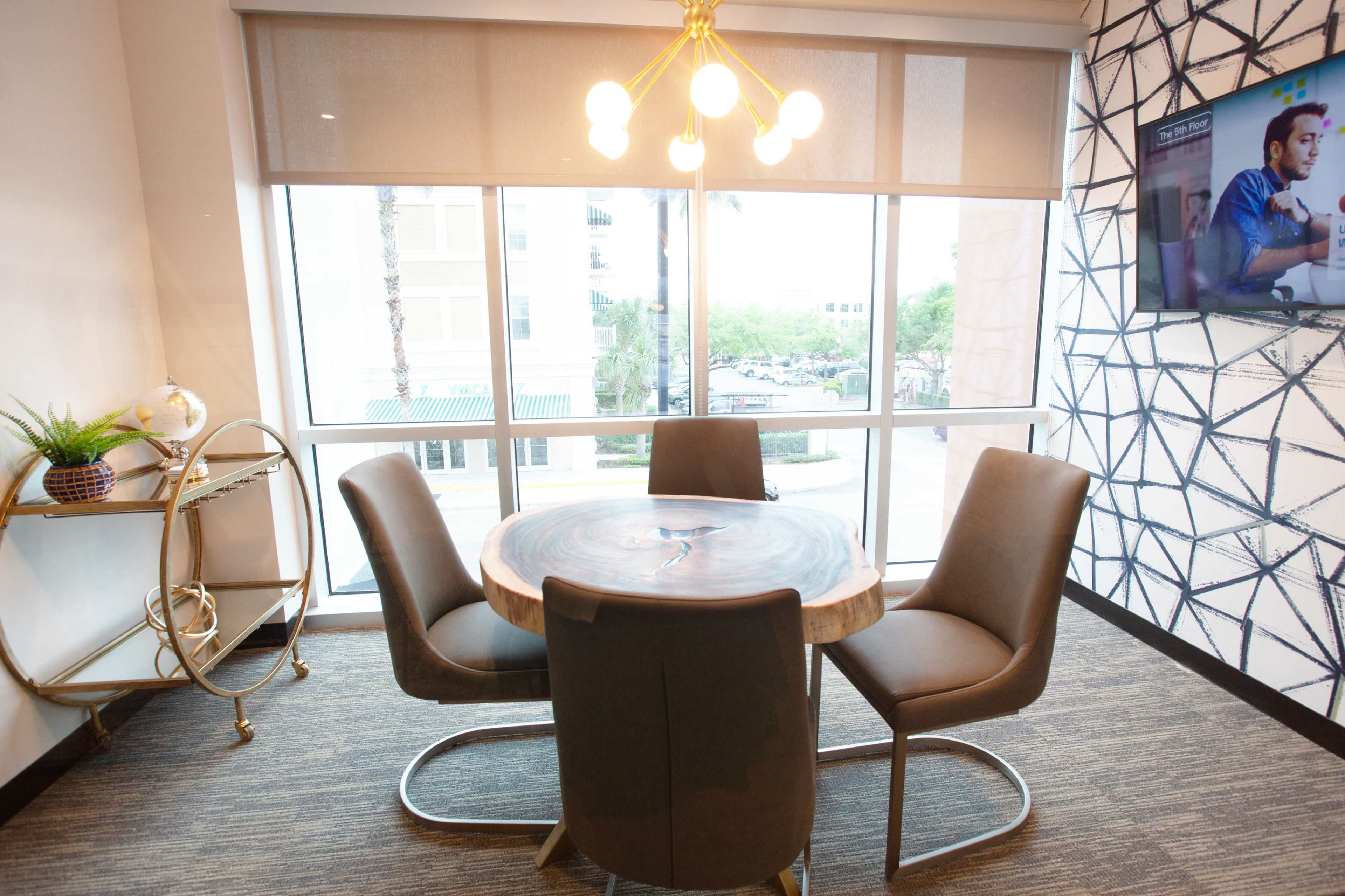 A modern dining area with a round wooden table surrounded by four upholstered chairs, a golden cart beside it, and a large window providing natural light.