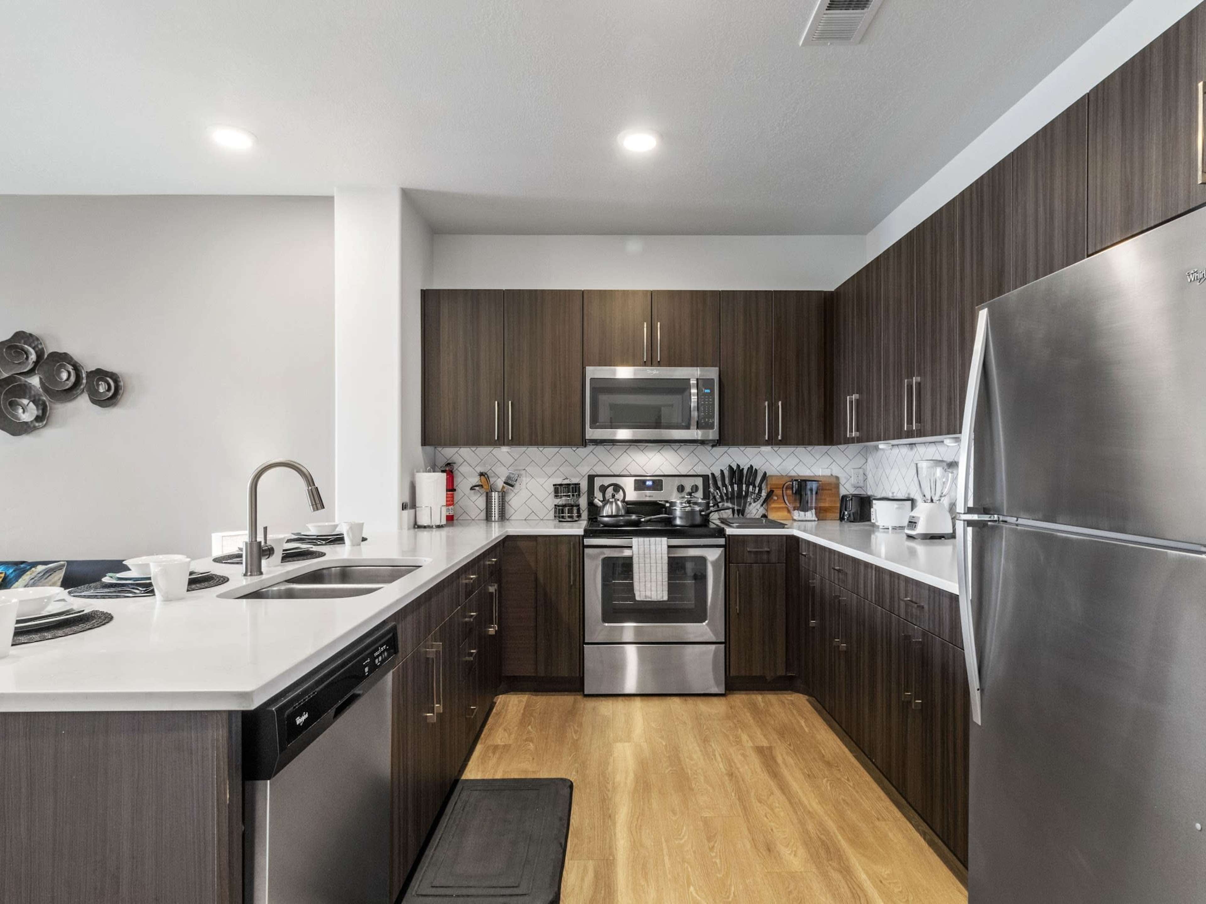A modern kitchen featuring dark wood cabinets, stainless steel appliances, and a white countertop.