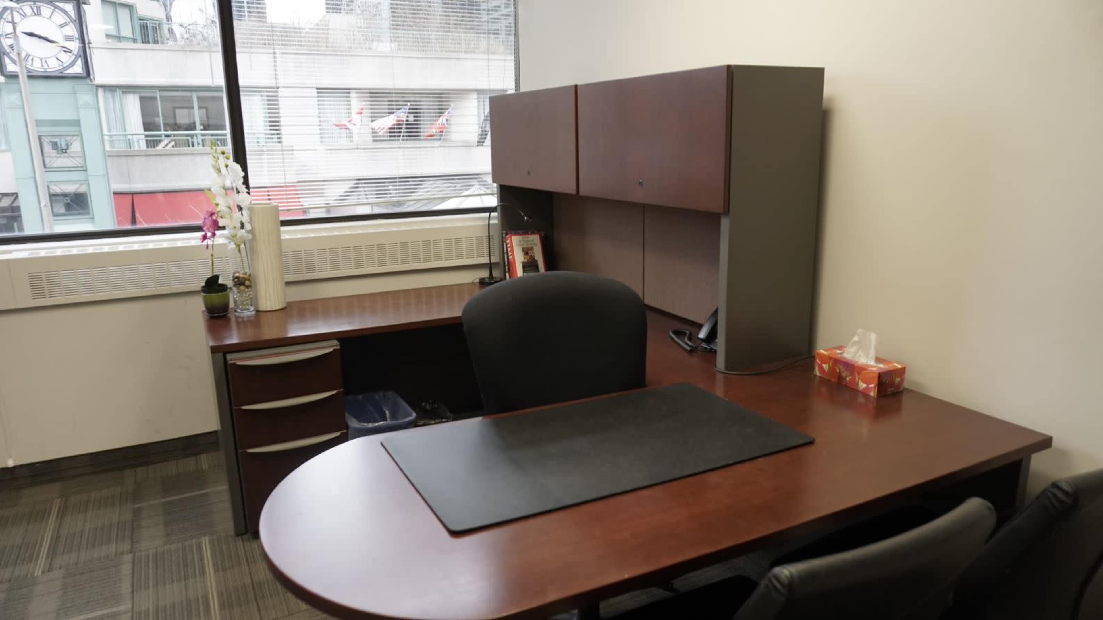 A modern office space featuring a wooden desk, an ergonomic chair, and a large window with a view of a building and parked cars.
