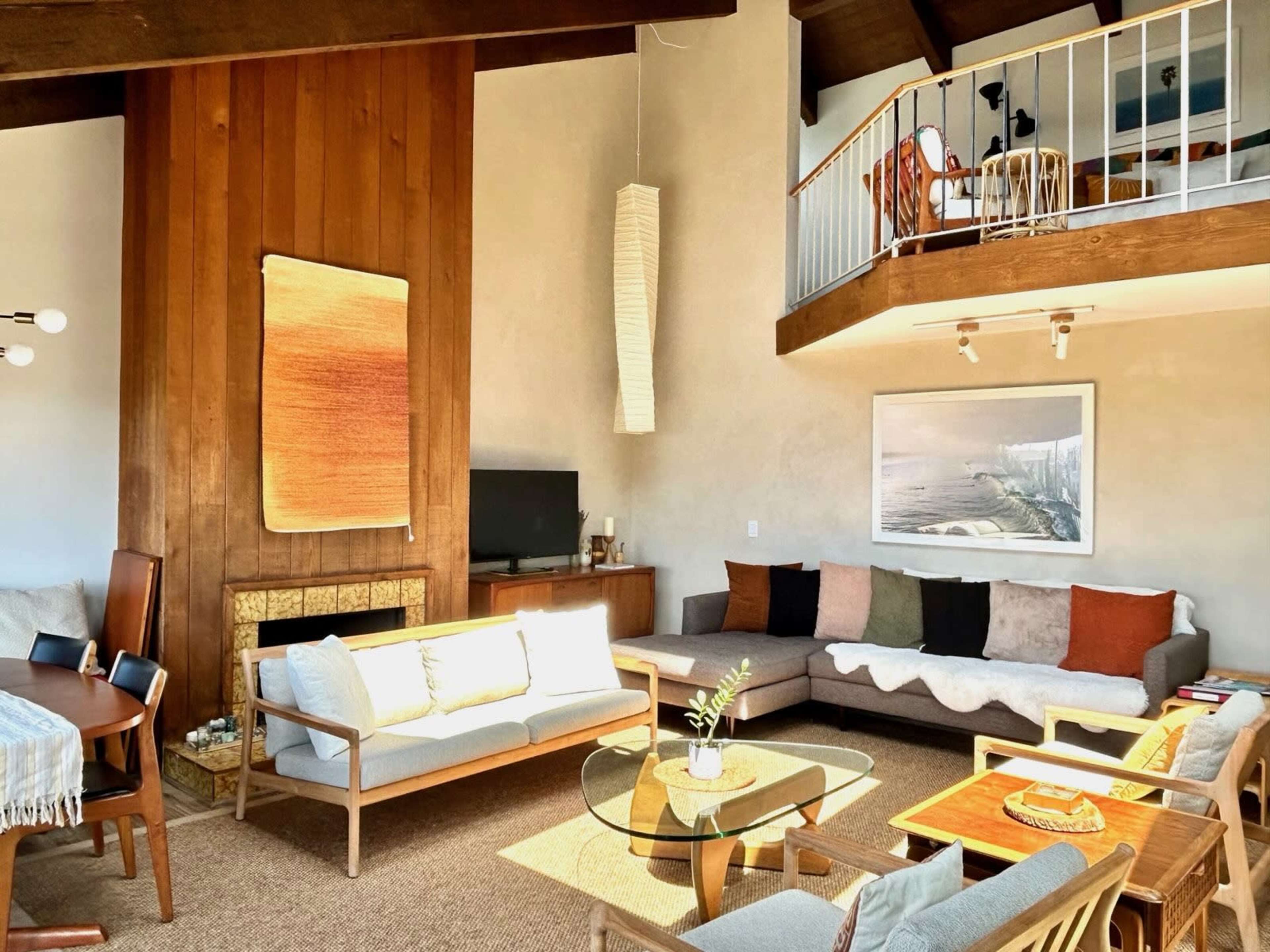 The living room features a modern design with a large window, a fireplace, sofas, a coffee table, and a dining area in an open layout.