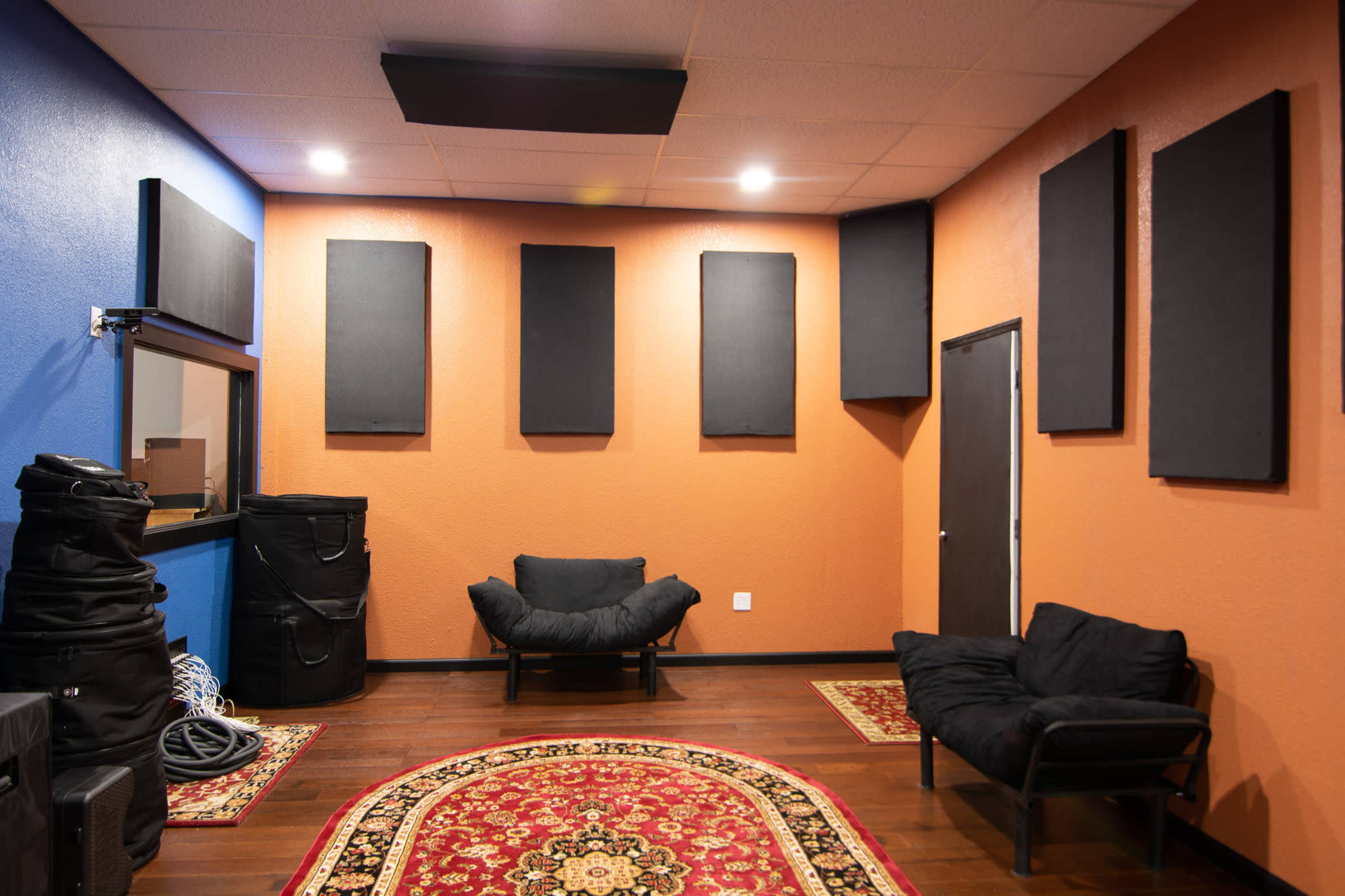 A soundproof room featuring two black couches, a patterned rug, and acoustic panels mounted on the orange and blue walls.