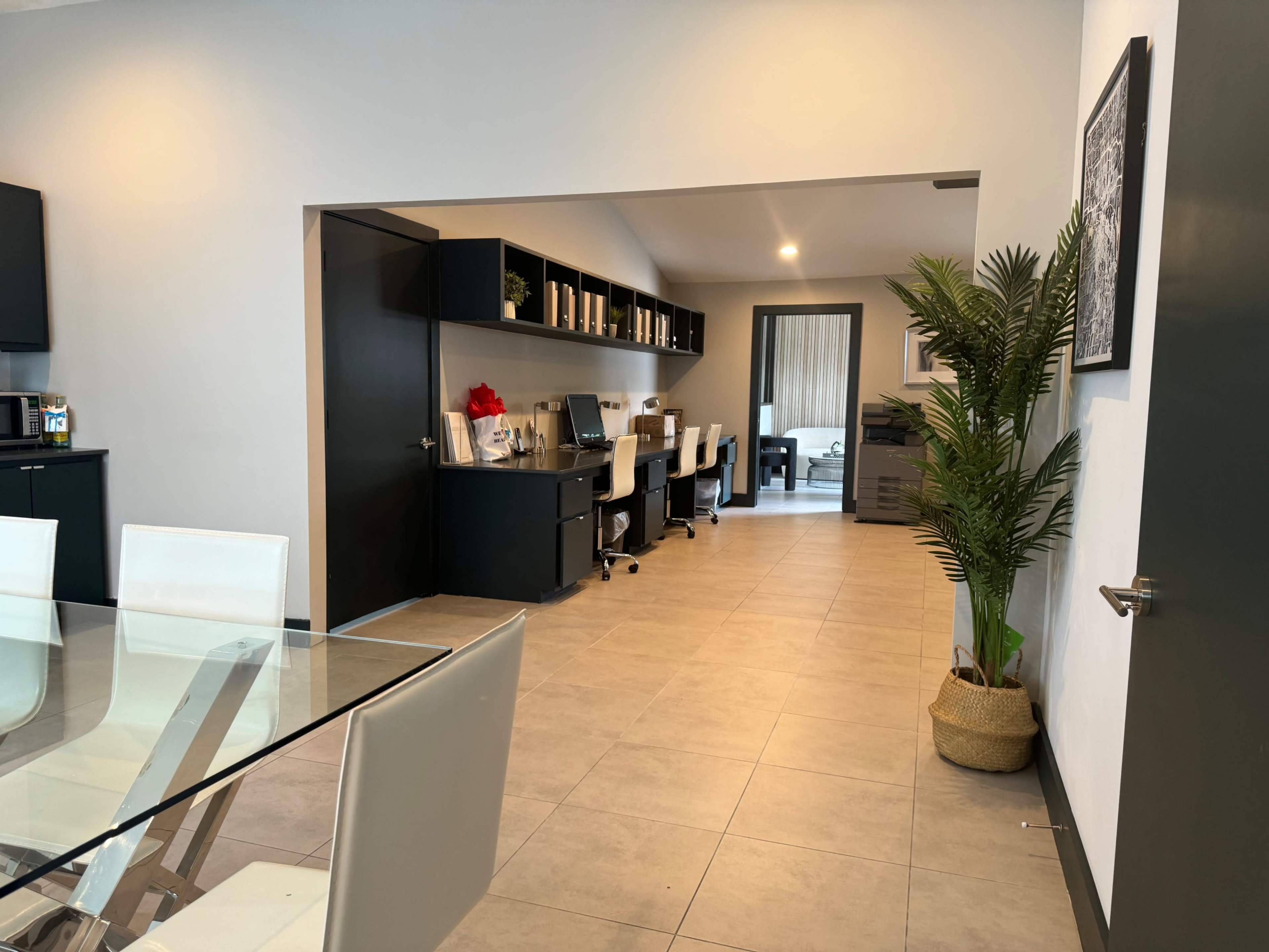 The image shows a modern office space featuring a dining table in the foreground and multiple workstations with chairs in the background.