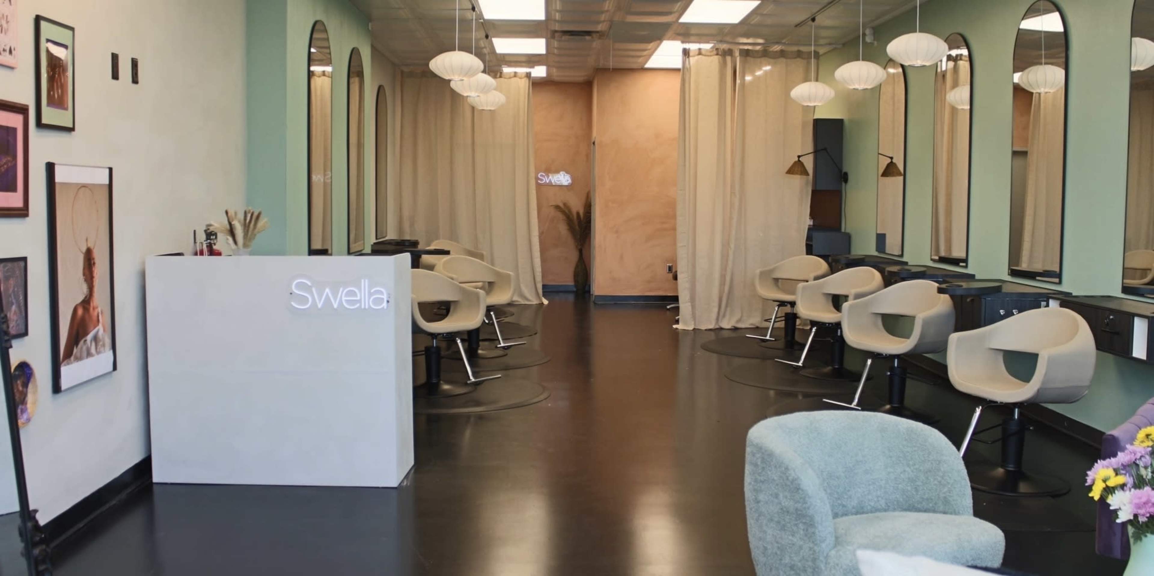 The image shows a modern hair salon interior with a reception desk, salon chairs arranged in a row, and decorative elements on the walls.