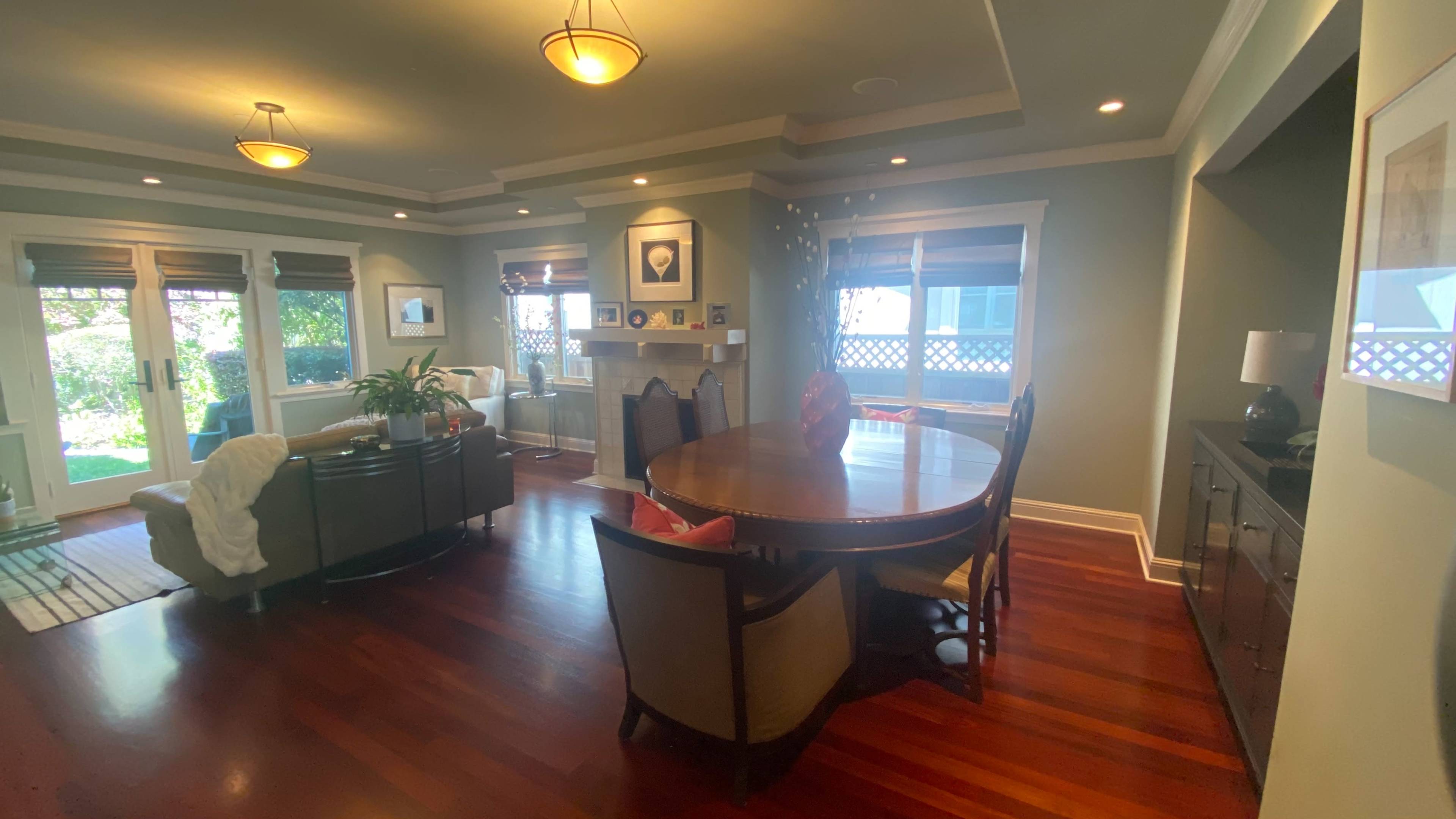 A living area with a round dining table surrounded by chairs, a sofa, and a fireplace, illuminated by pendant lights.
