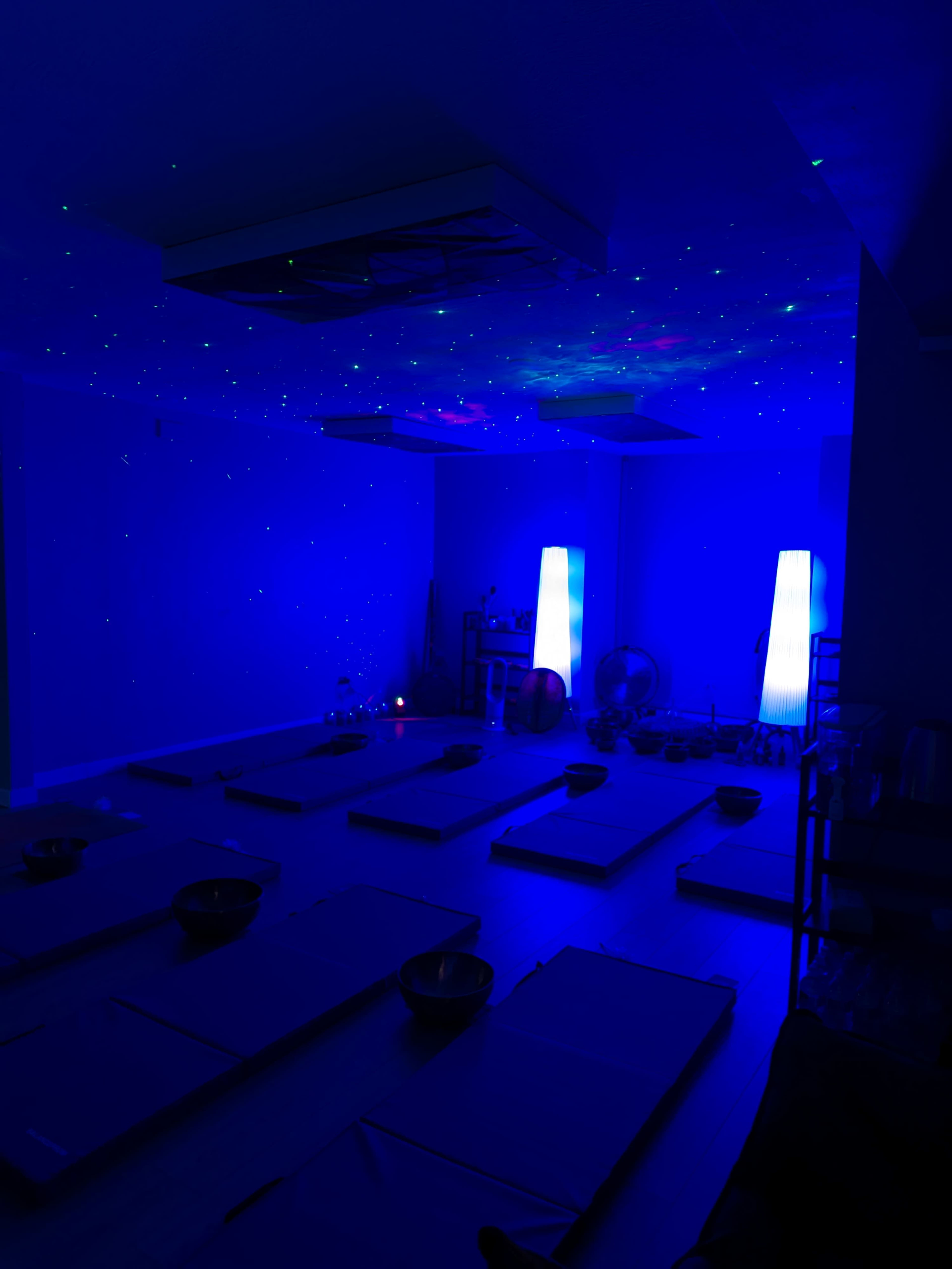A dimly lit room with blue lighting features yoga mats arranged on the floor and illuminated lamps on either side.