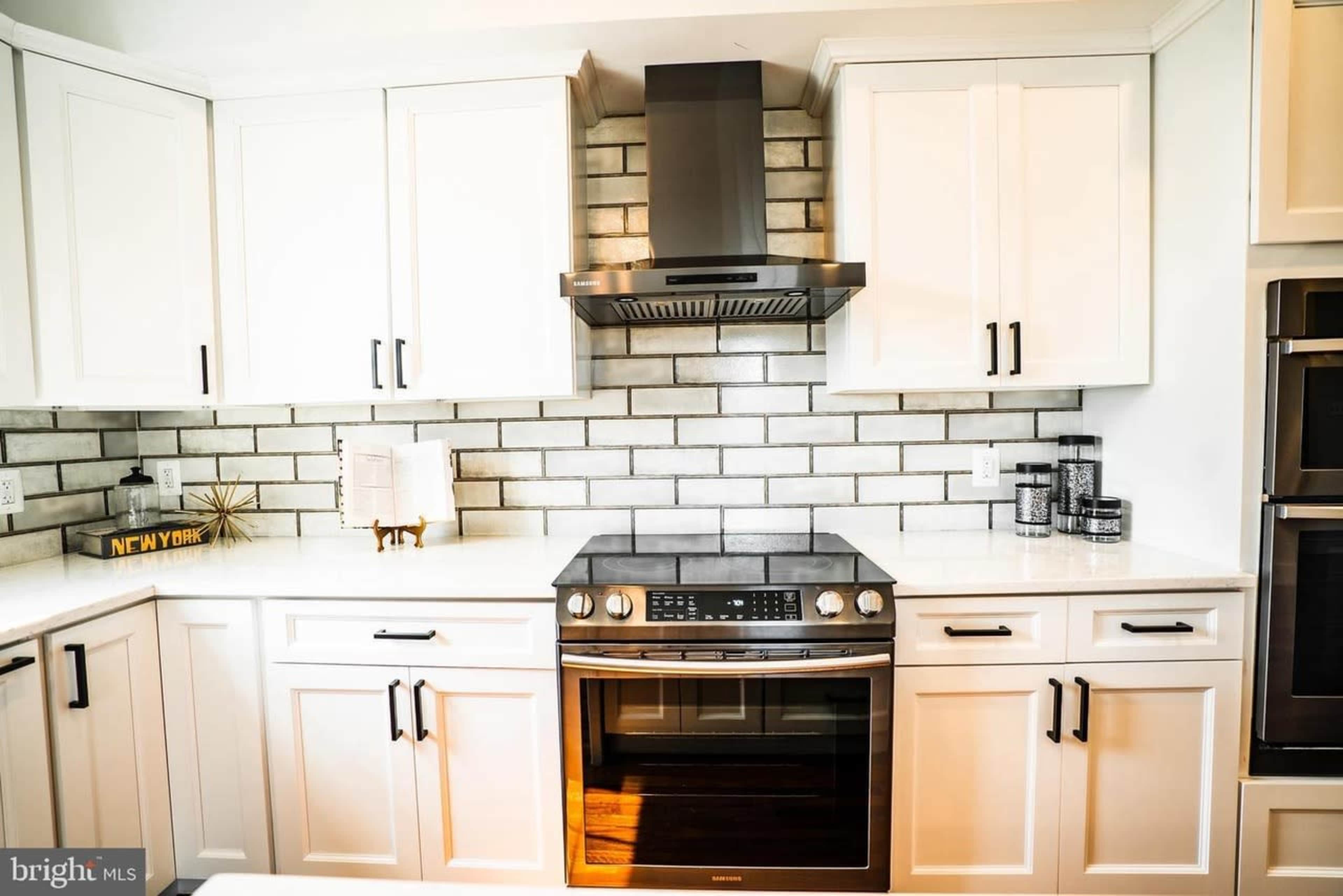 The kitchen features white cabinets, a stainless steel oven, a tile backsplash, and a range hood.