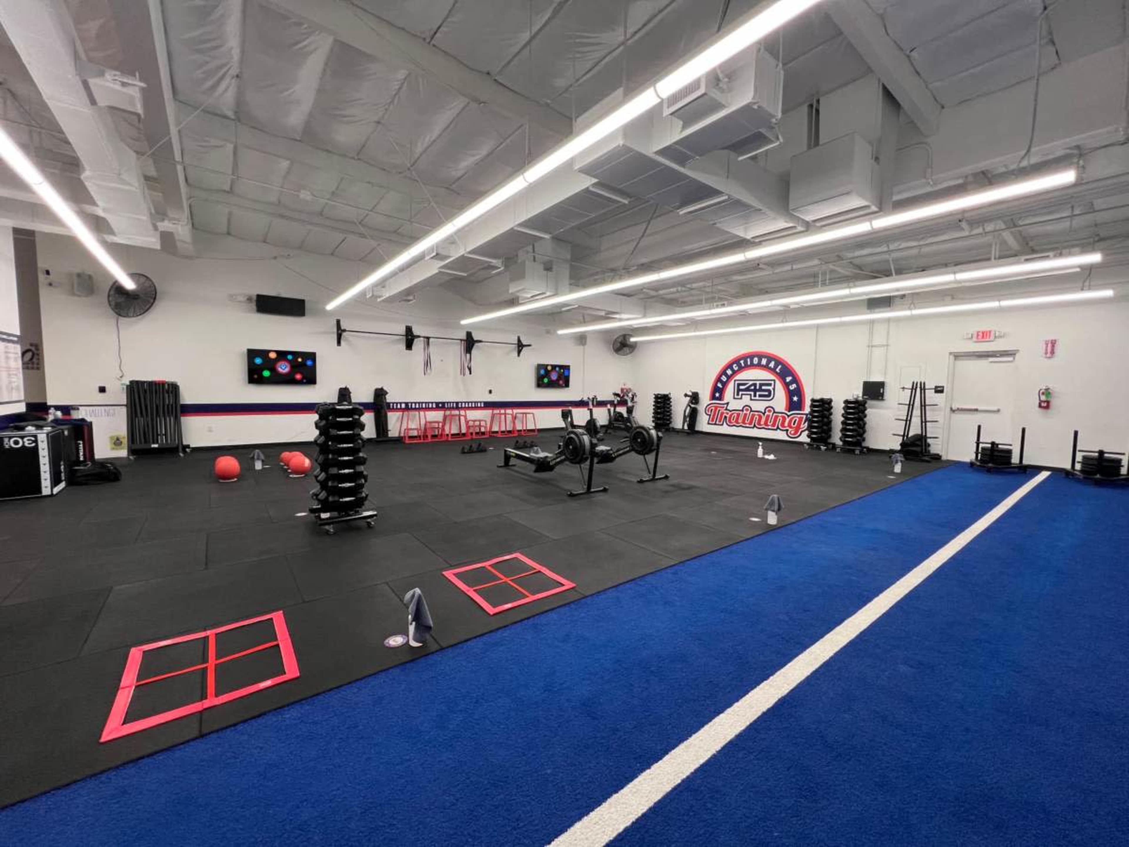 The image shows a spacious gym with black rubber flooring, organized weights, exercise equipment, and a blue running lane.
