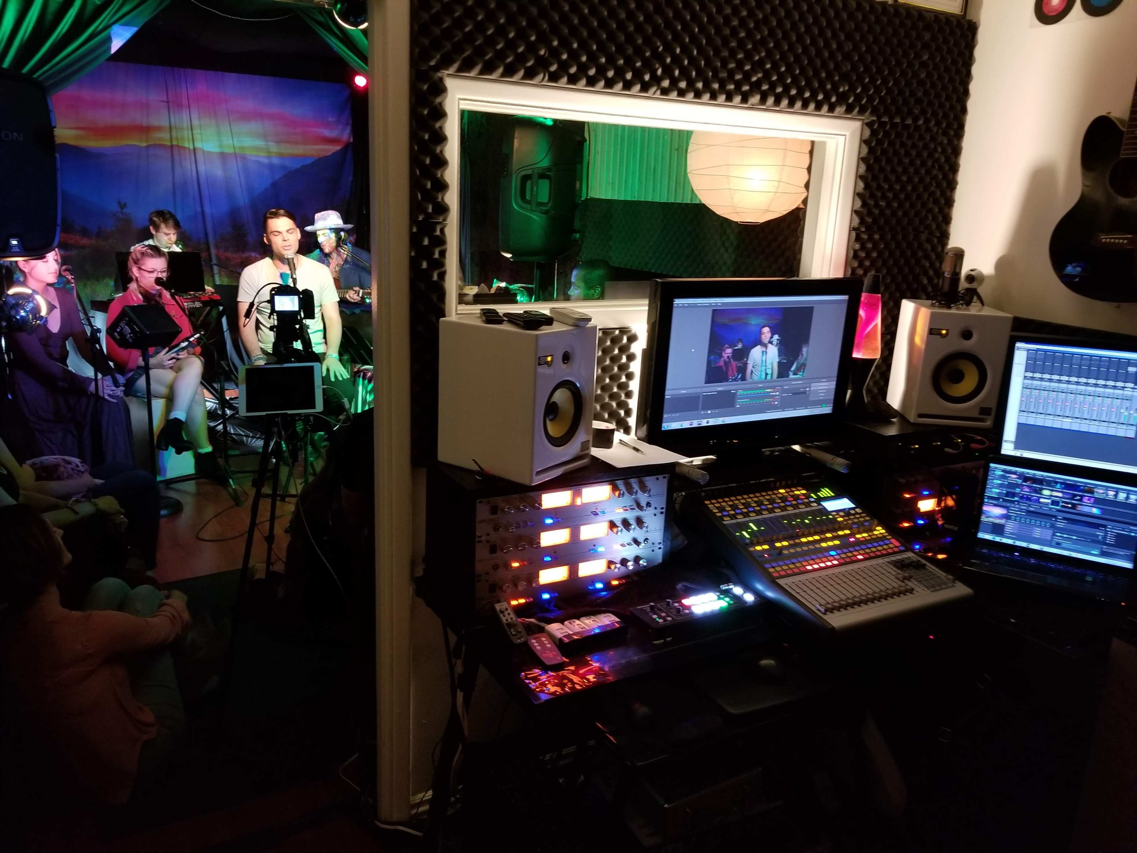 A recording studio with a control desk featuring monitors and audio equipment, while a small live band performs in the background.